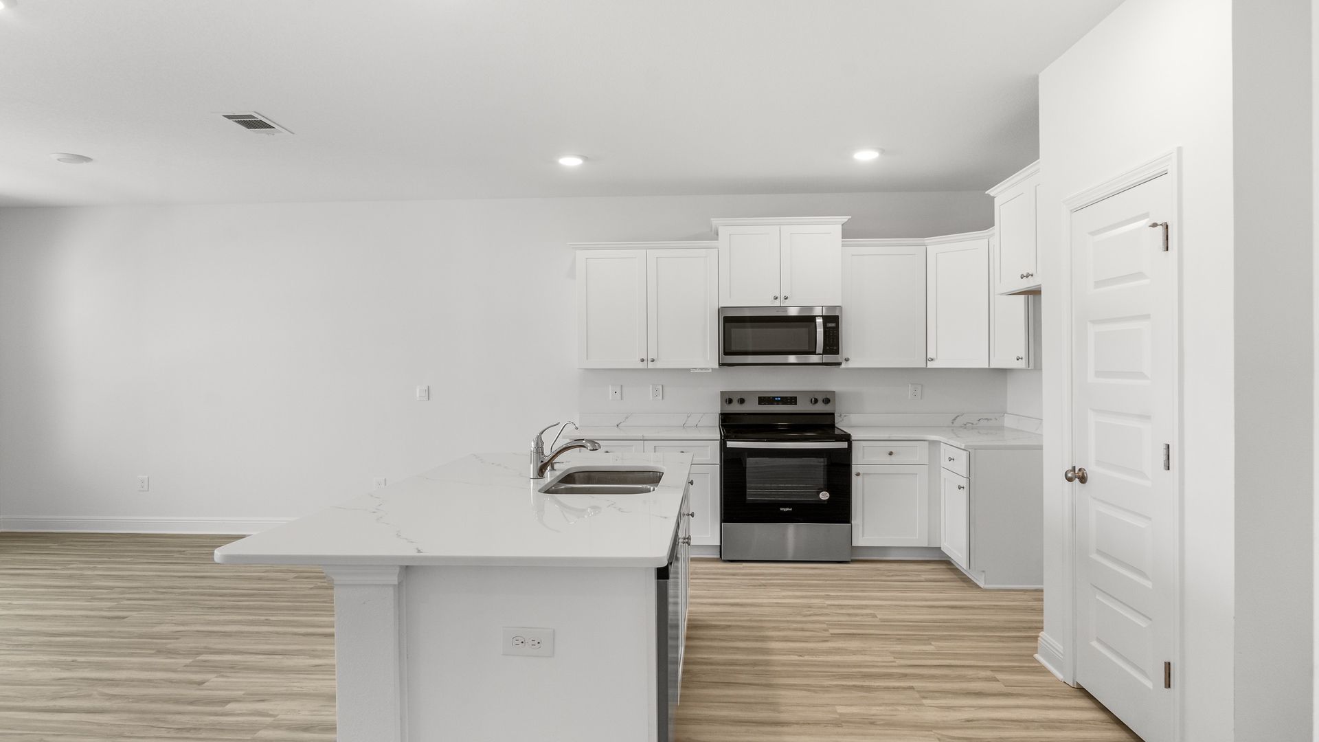 Kitchen with quartz countertops and stainless-steel appliances and island and white cabinets.