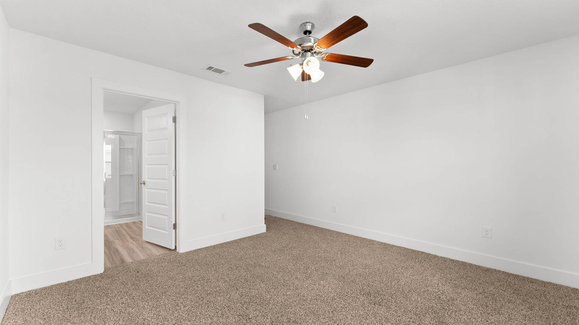 Primary bedroom with ceiling fan and carpet flooring and bathroom entrance.