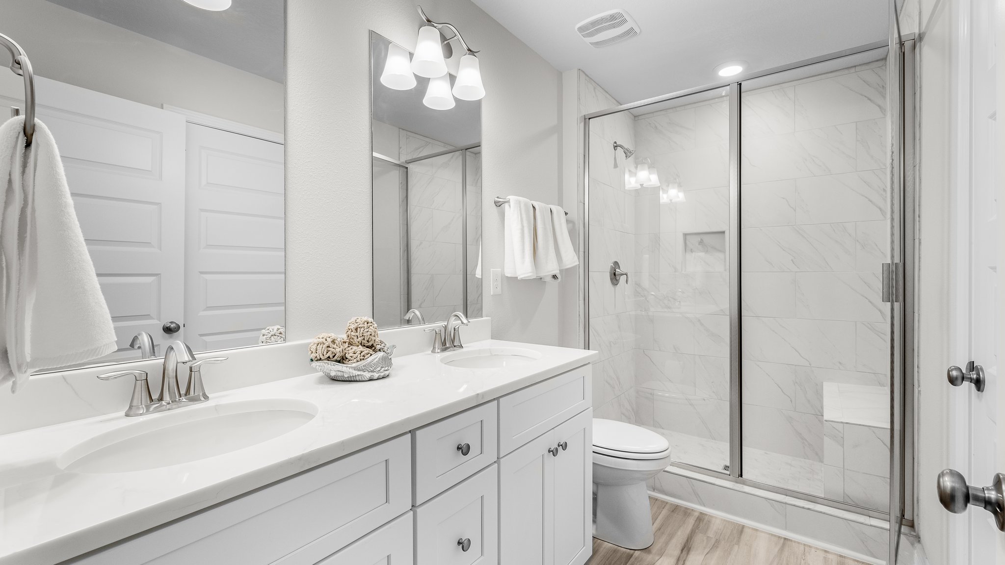 Primary bathroom with double vanity quartz countertops and toilet and tile shower with glass doors.
