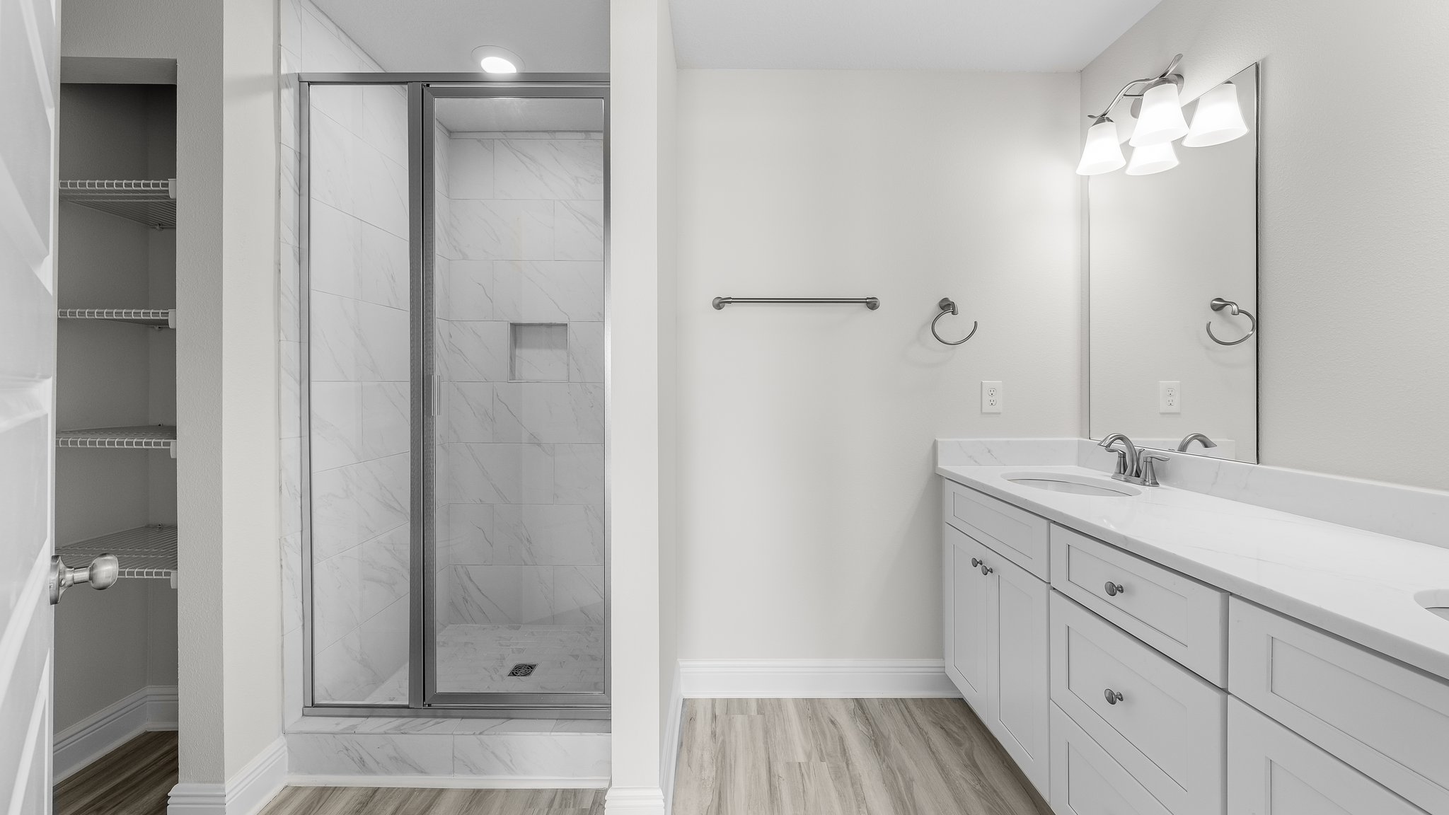 Primary bathroom with tile shower with glass doors and double vanity quartz countertops with white cabinets and EVP flooring.