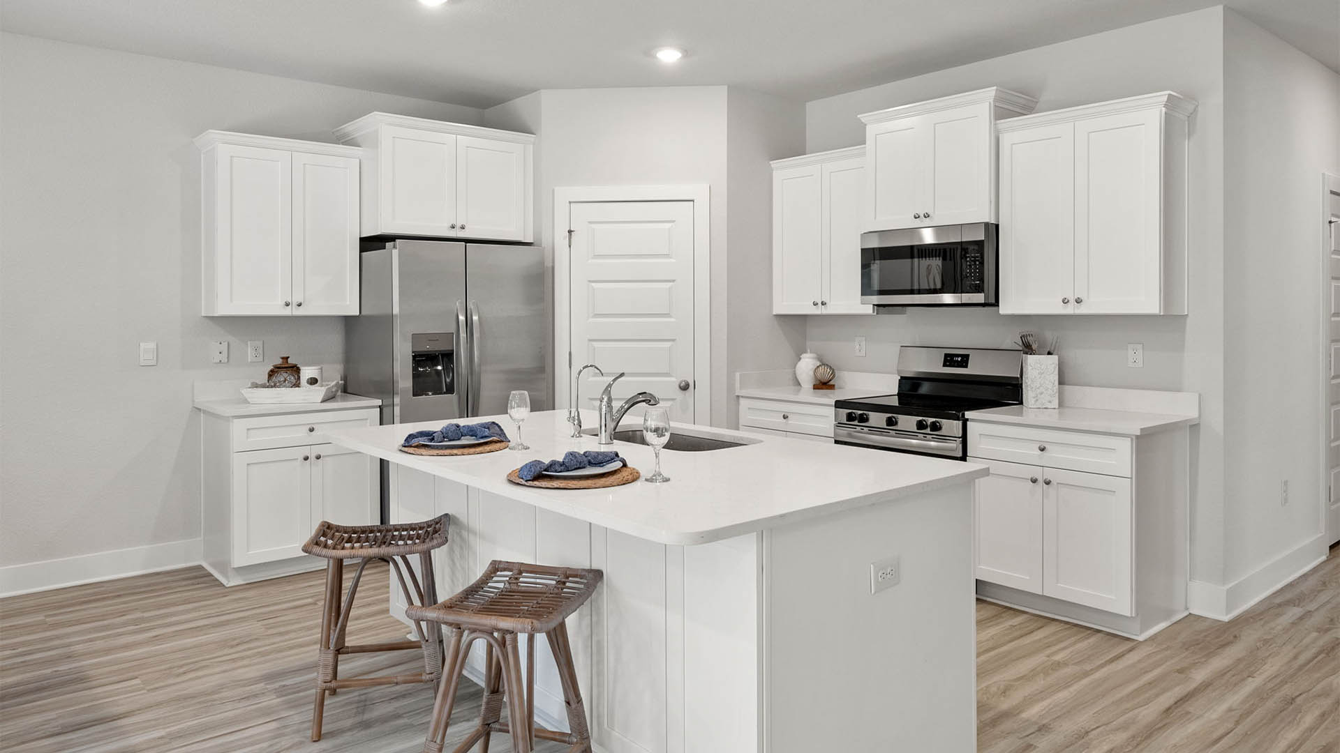 Kitchen with quartz countertops and white cabinetry and island and stainless-steel appliances and pantry.