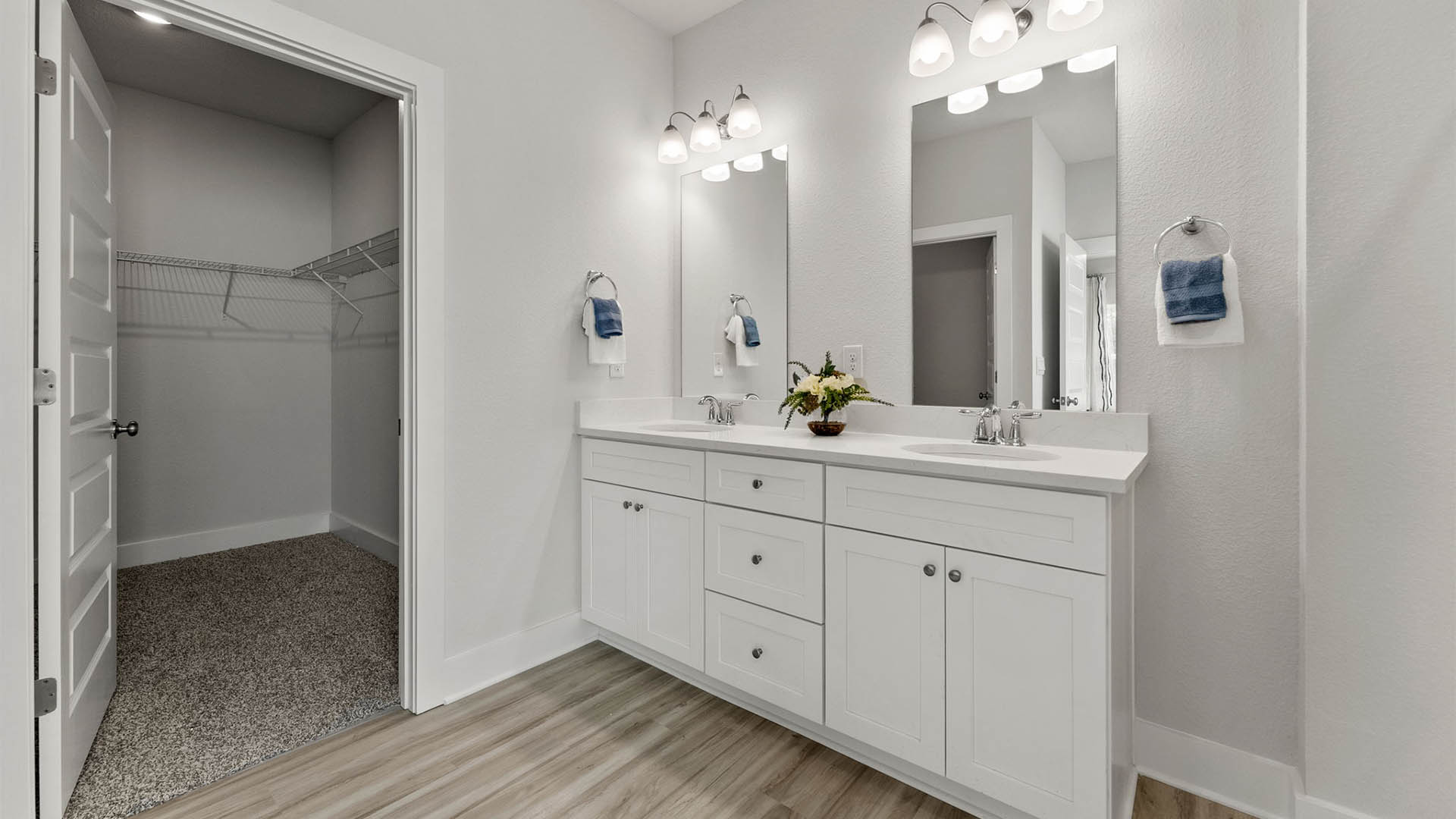 Primary bathroom with double vanity quartz countertops and EVP flooring and white cabinets and walk-in closet.