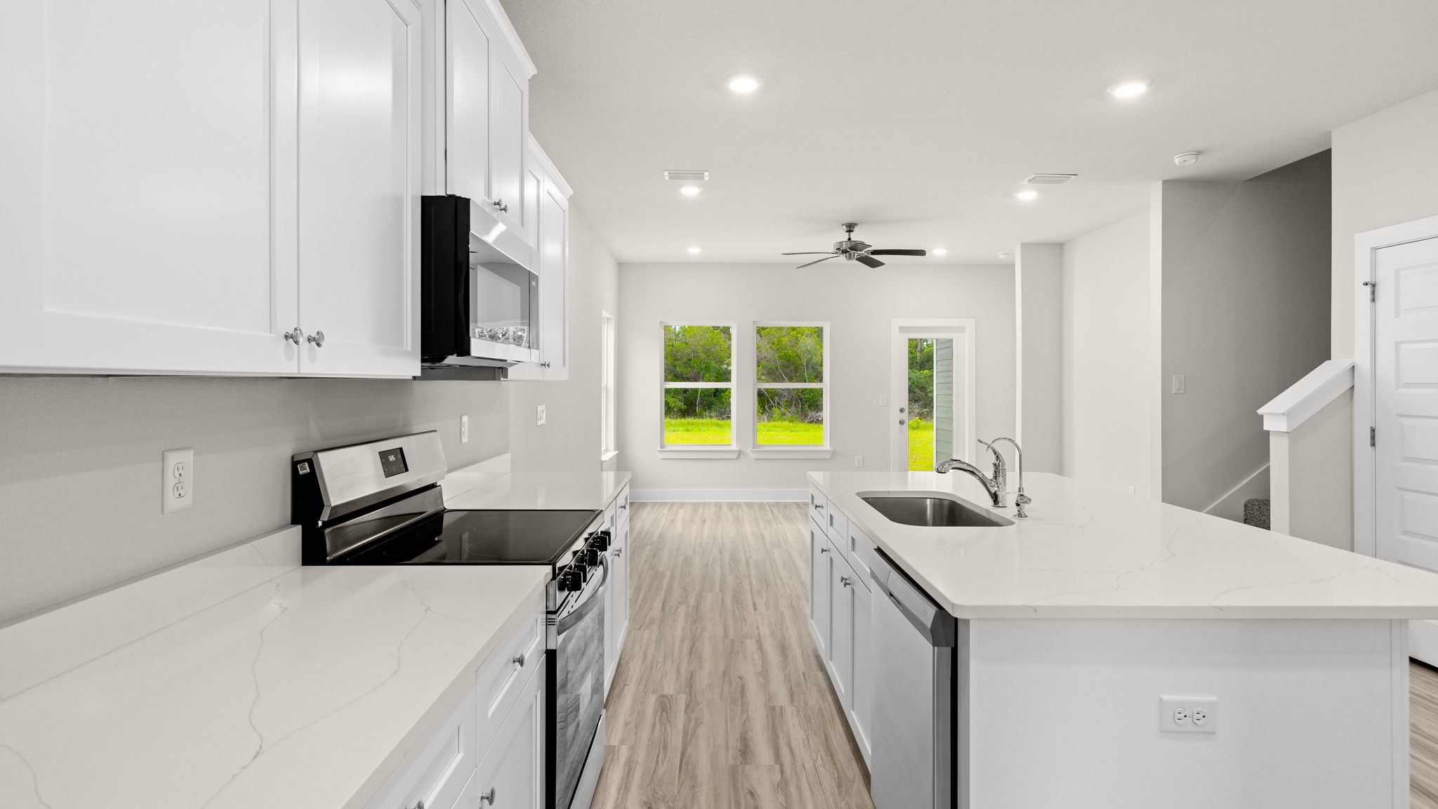 Kitchen with EVP flooring and quartz countertops and white cabinets and island and stainless-steel appliances.
