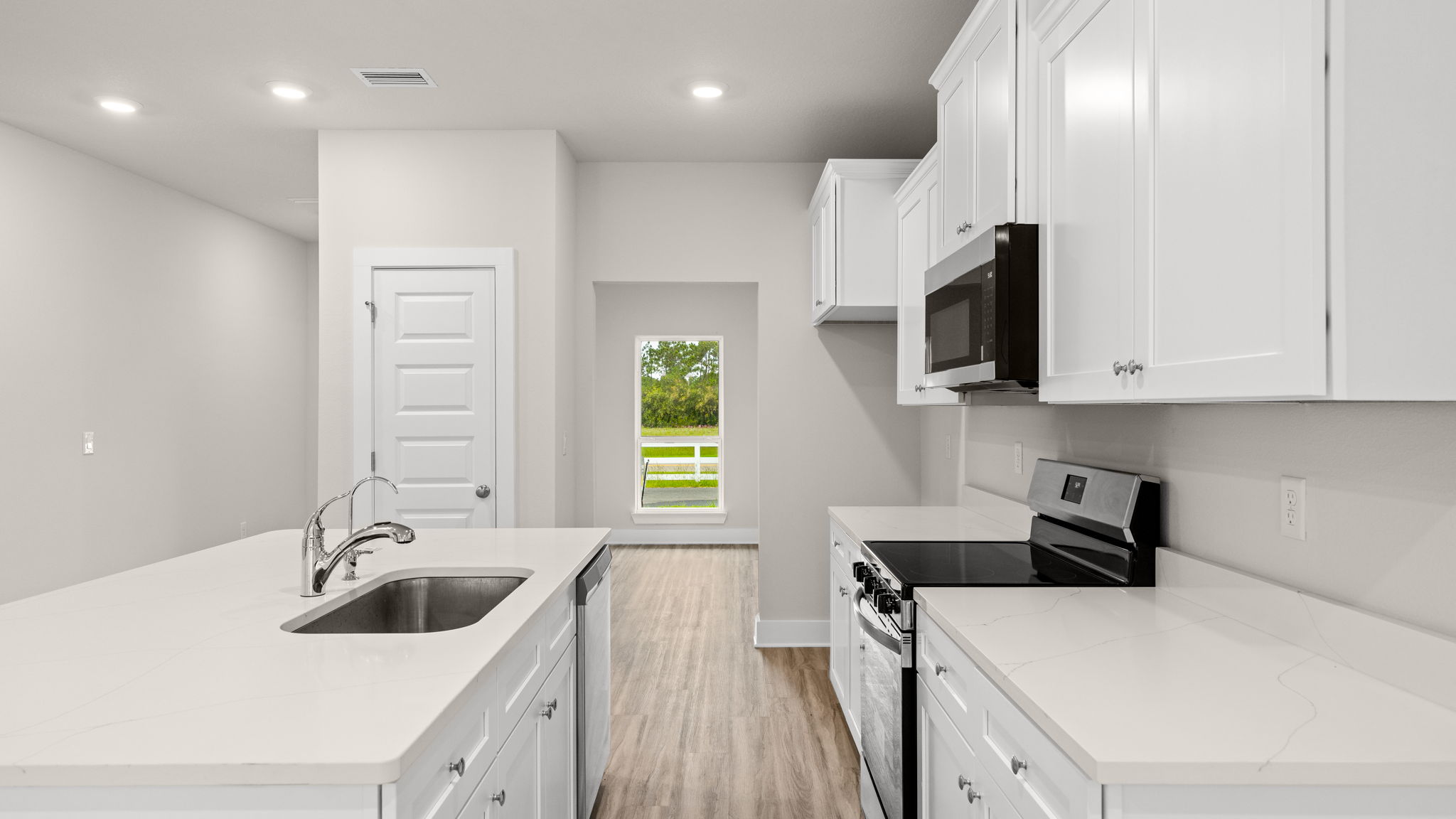 Kitchen with EVP flooring and quartz countertops and white cabinets and island and stainless-steel appliances.