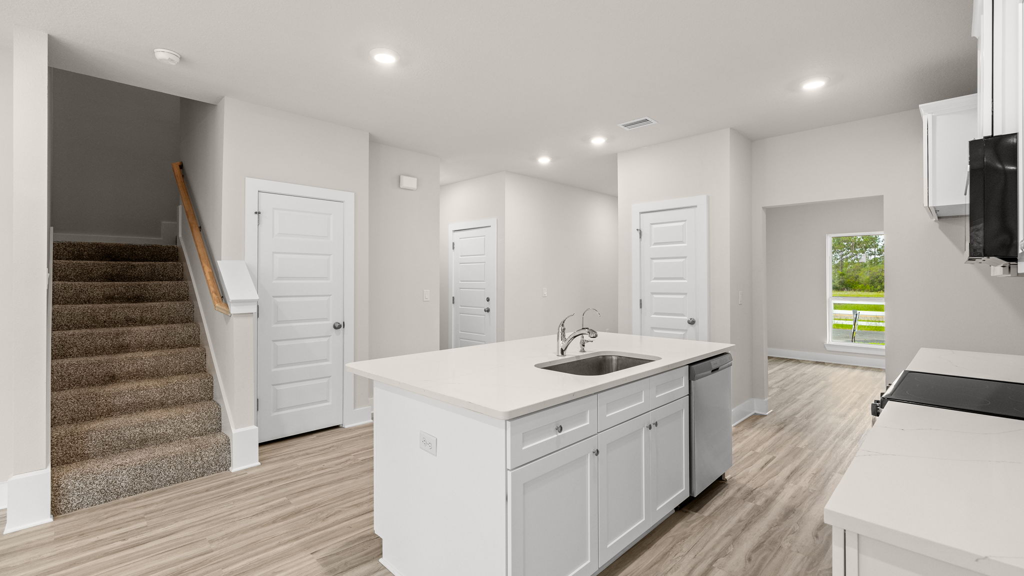 Kitchen with EVP flooring and quartz countertops and white cabinets and island and stainless-steel appliances.