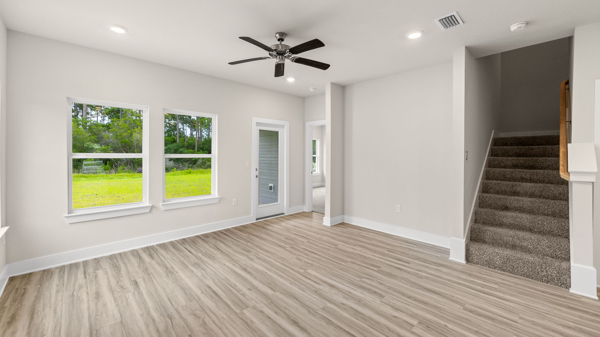 Living room with ceiling fan and EVP flooring and back door and stairs.