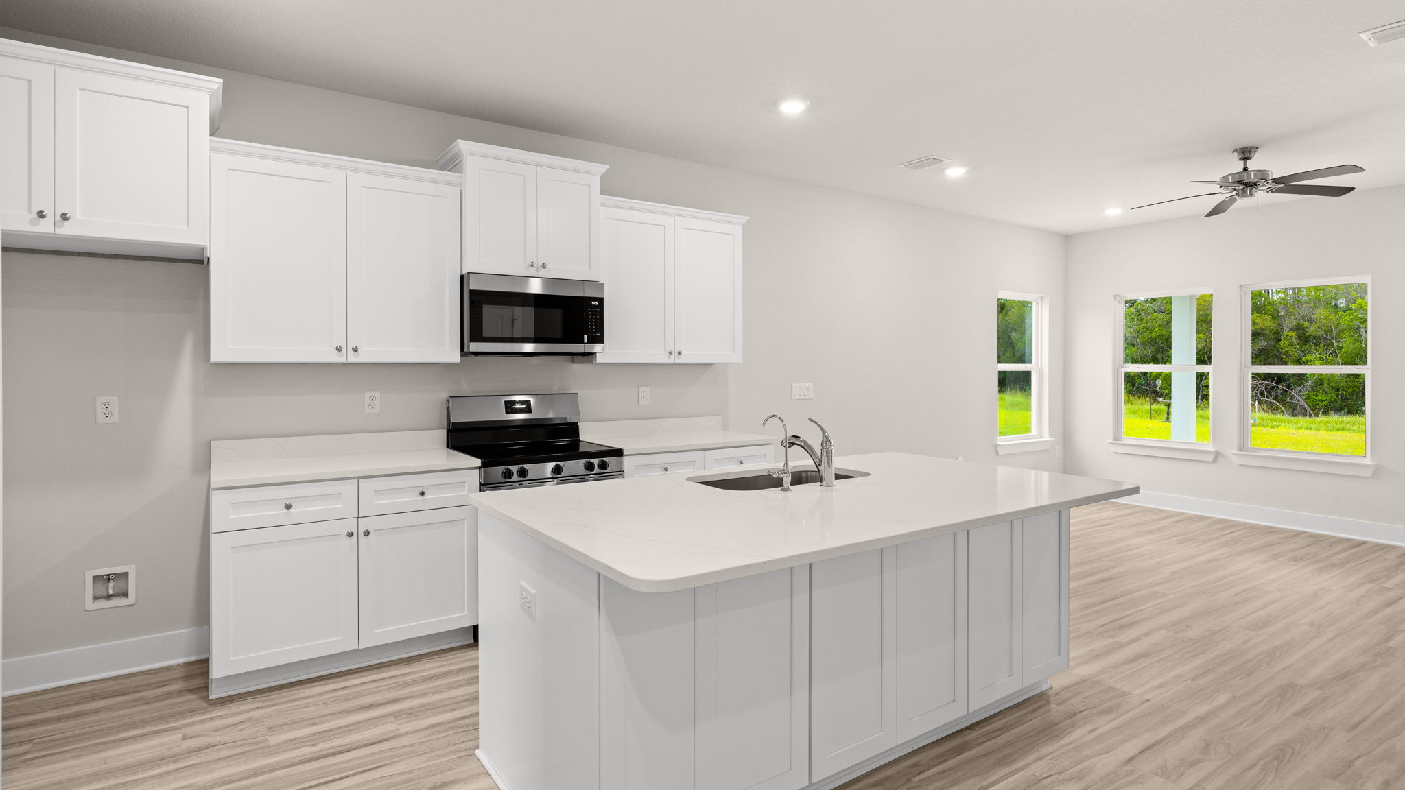 Kitchen with EVP flooring and quartz countertops and white cabinets and island and stainless-steel appliances.
