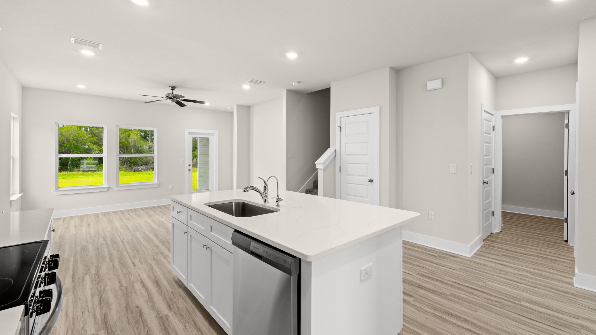 Kitchen with EVP flooring and quartz countertops and white cabinets and island and stainless-steel appliances.