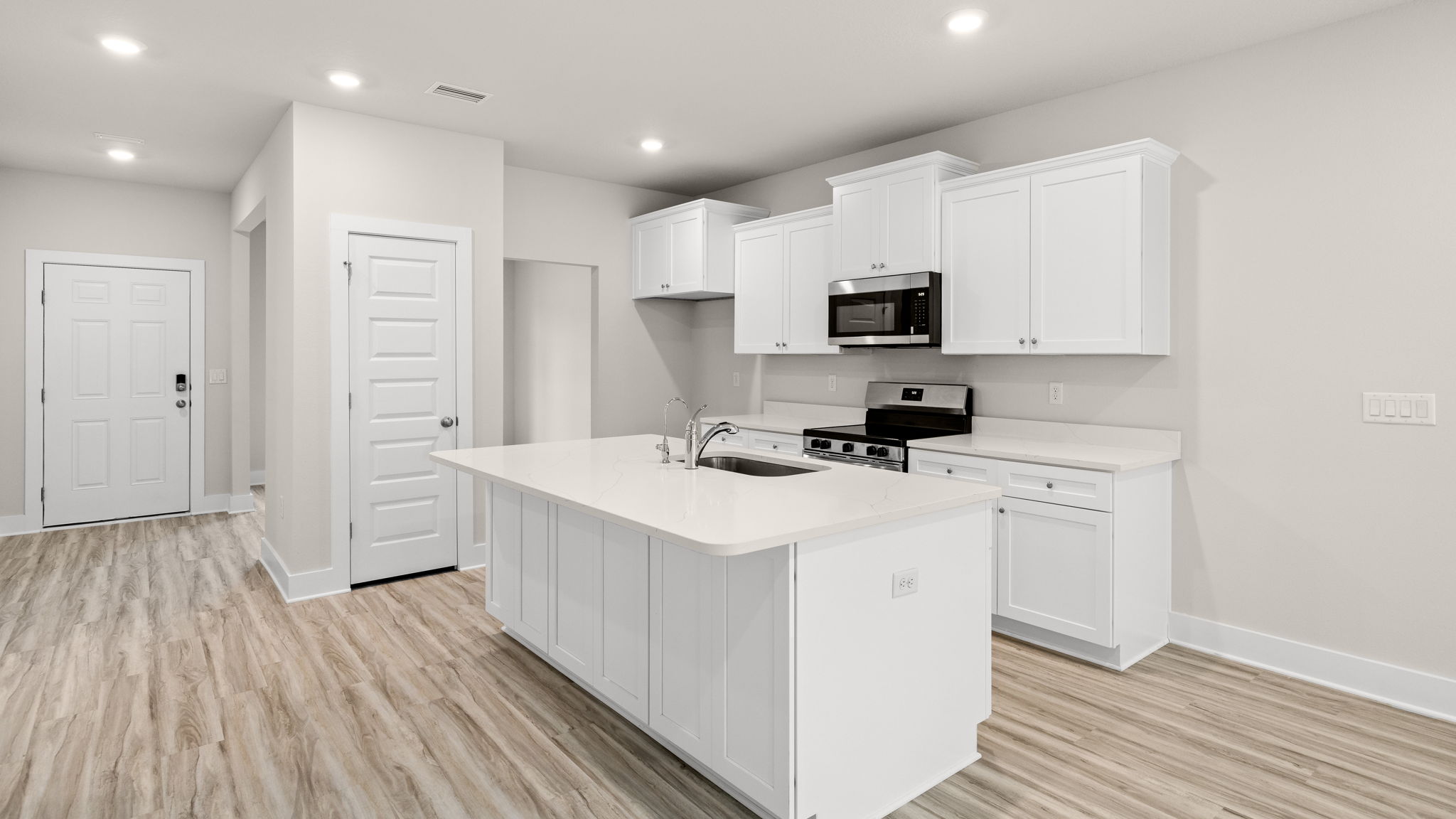 Kitchen with EVP flooring and quartz countertops and white cabinets and island and stainless-steel appliances.