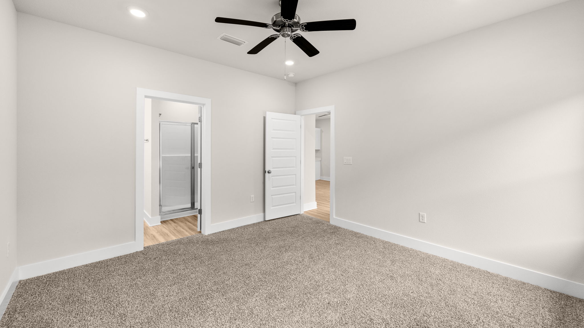 Primary bedroom with carpet flooring with ceiling fan and window and bathroom entrance.