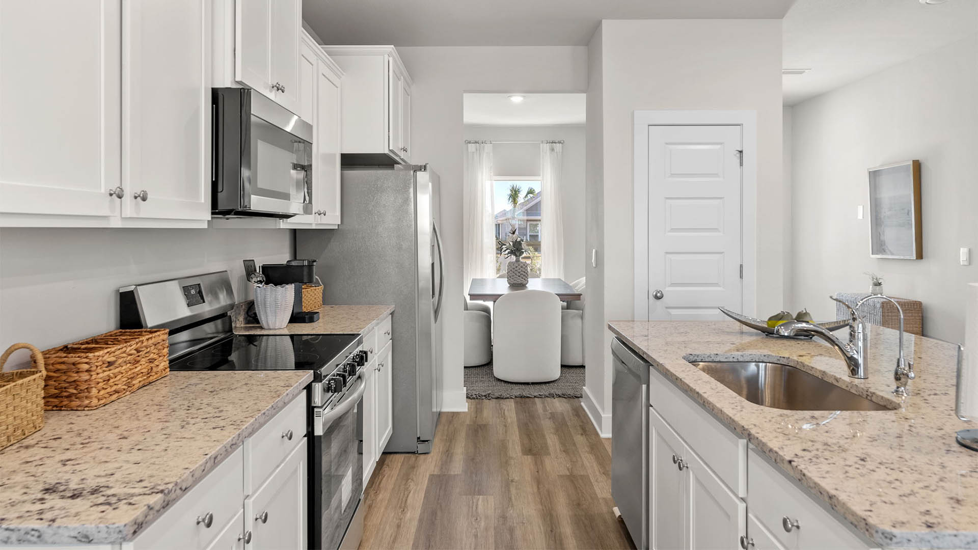 Kitchen with EVP flooring and granite countertops and white cabinets and island and stainless-steel appliances.