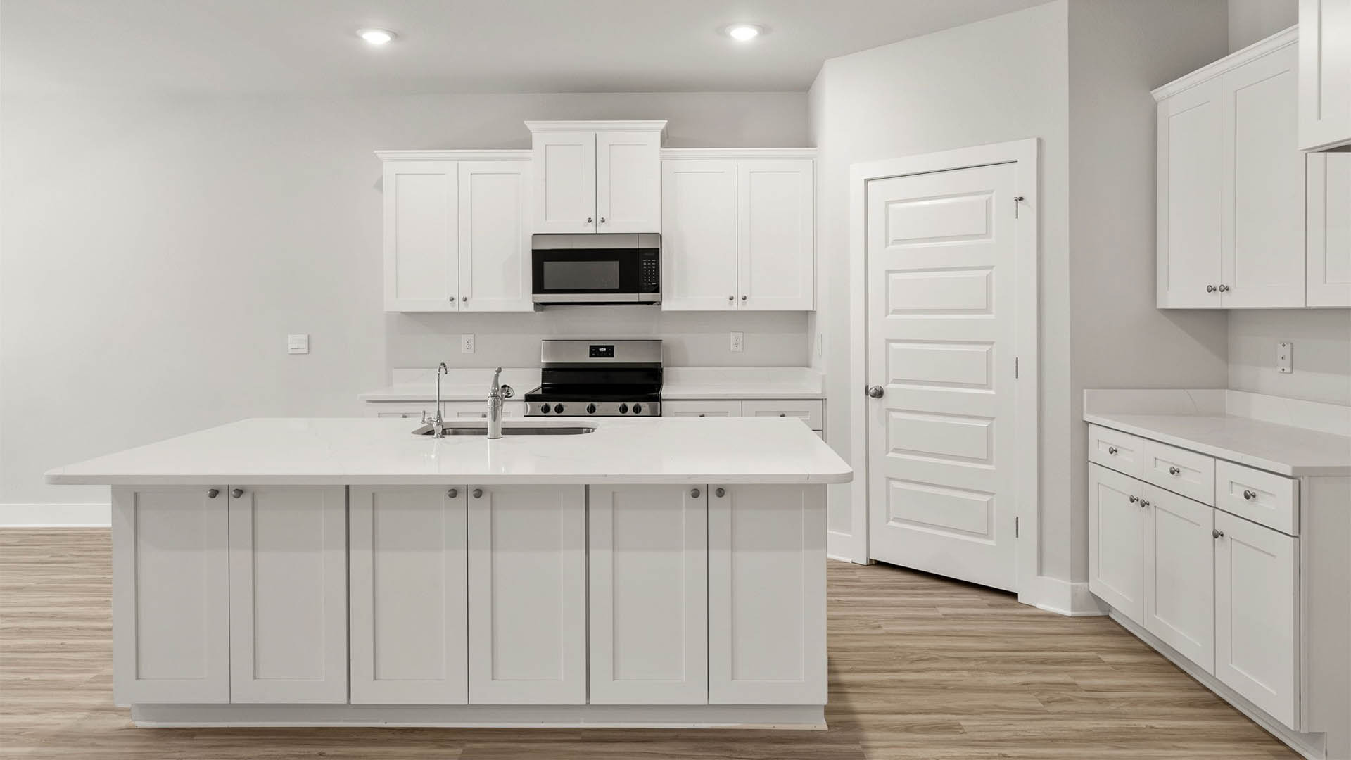 Open kitchen with island with white cabinets and quarts countertops and pantry and EVP flooring.