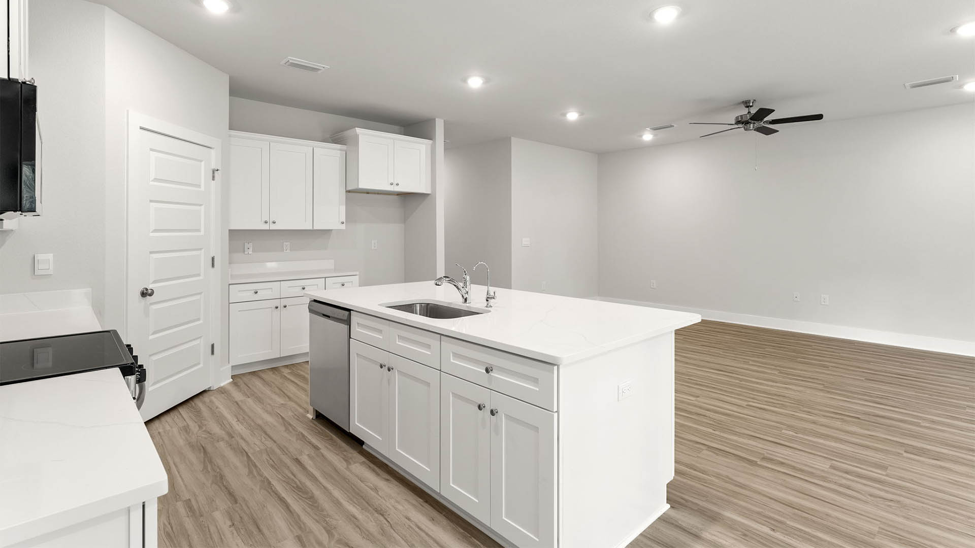 Open kitchen with island with white cabinets and quarts countertops and pantry and EVP flooring.