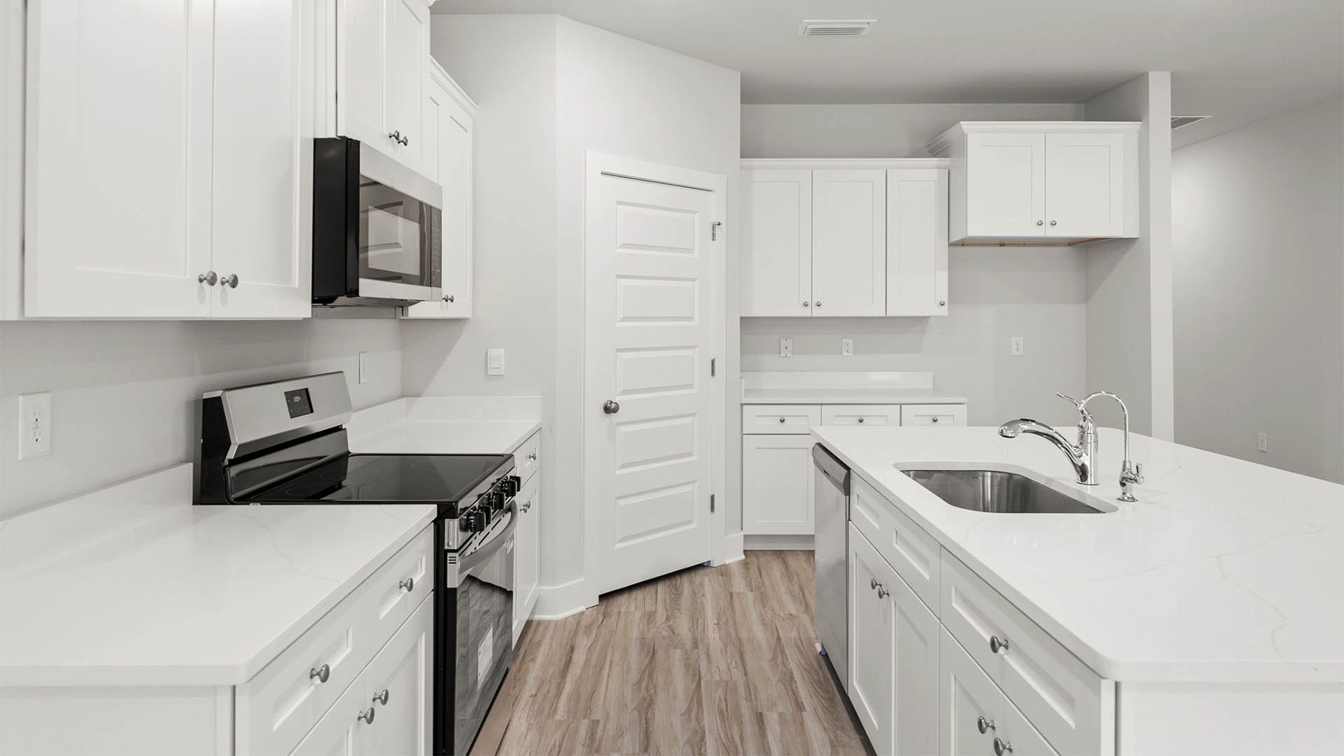 Open kitchen with island with white cabinets and quarts countertops and pantry and EVP flooring.