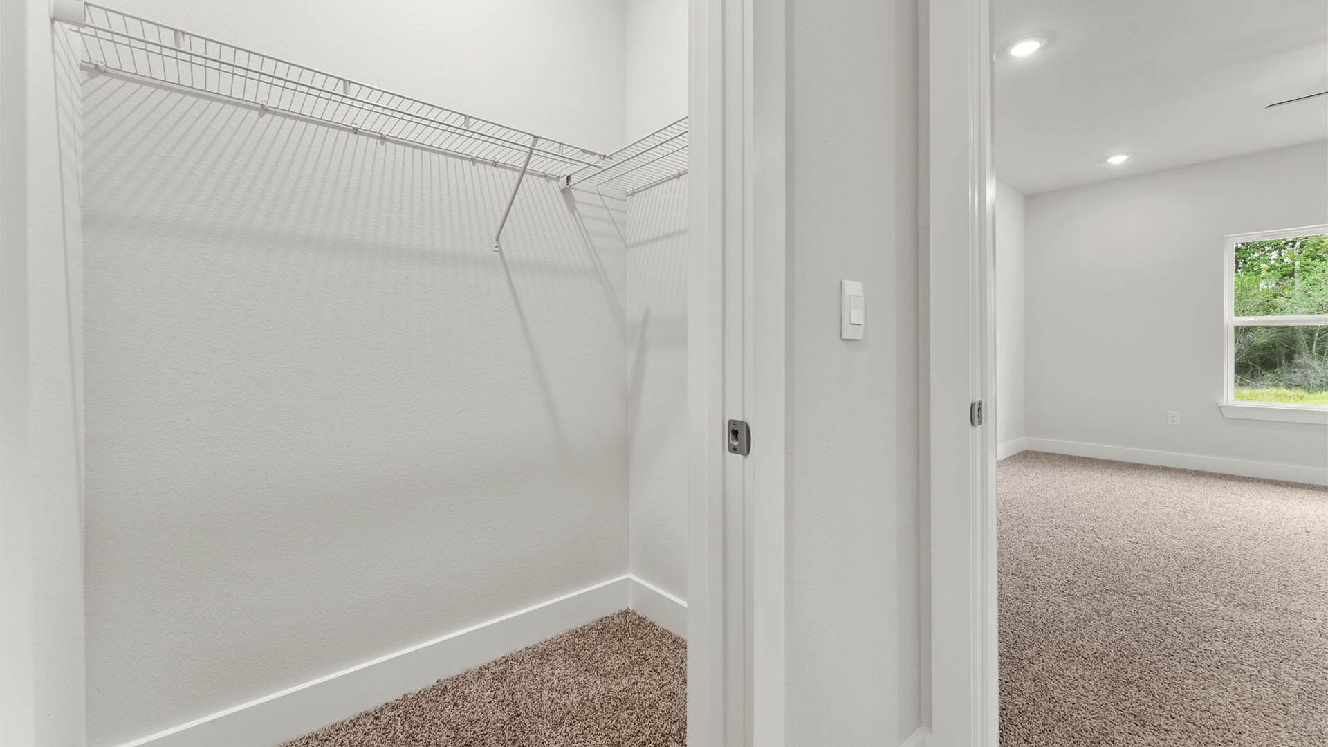 Primary bathroom closet with carpet floor and ventilated shelving and bedroom entrance.