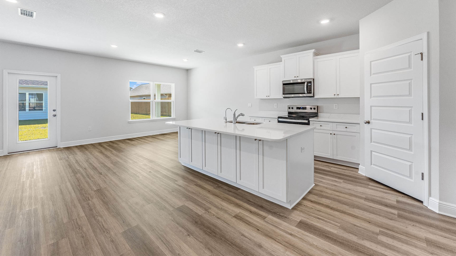 Open kitchen with island with white cabinets and quarts countertops and pantry and EVP flooring.