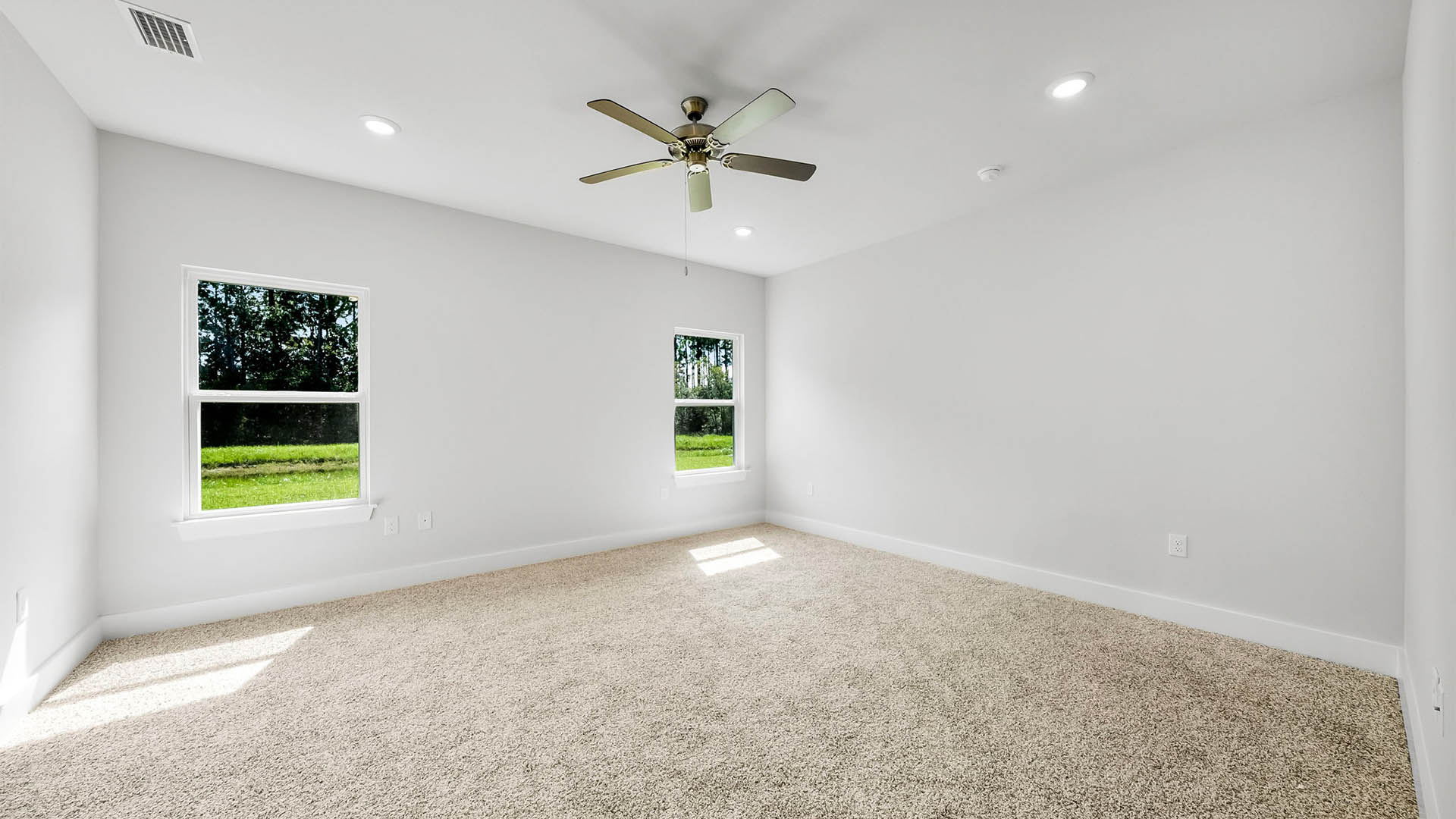 Primary bedroom with carpet flooring and ceiling fan and two windows.