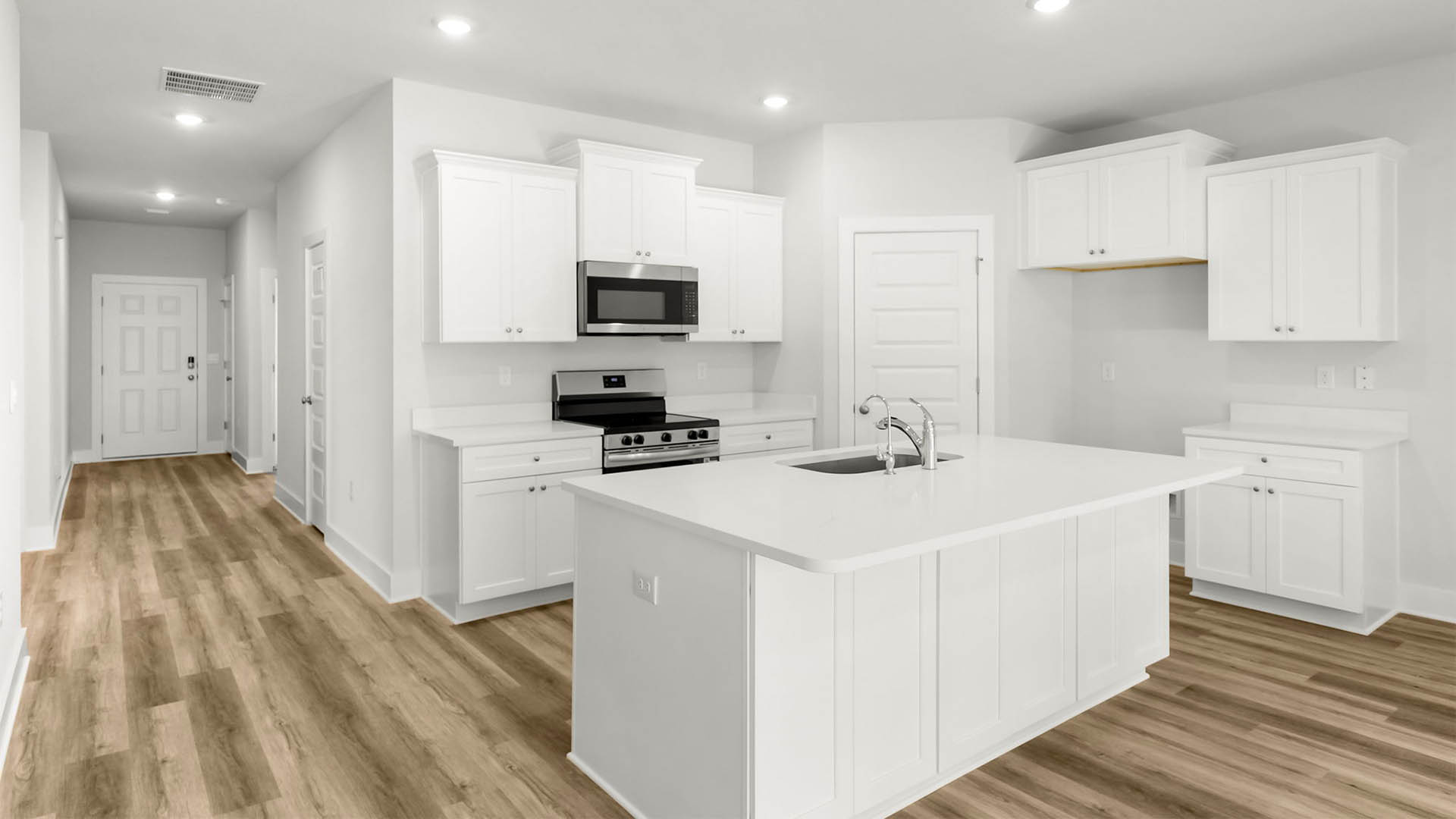 Kitchen with quartz countertops and white cabinetry and island and stainless-steel appliances and pantry.