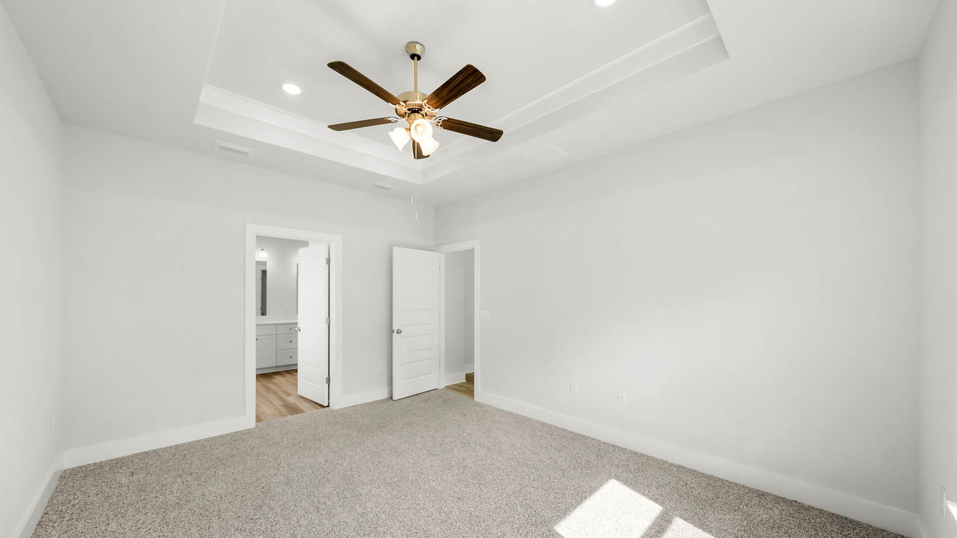 Primary bedroom with carpet floor and tray ceilings and ceiling fan bathroom entrance.
