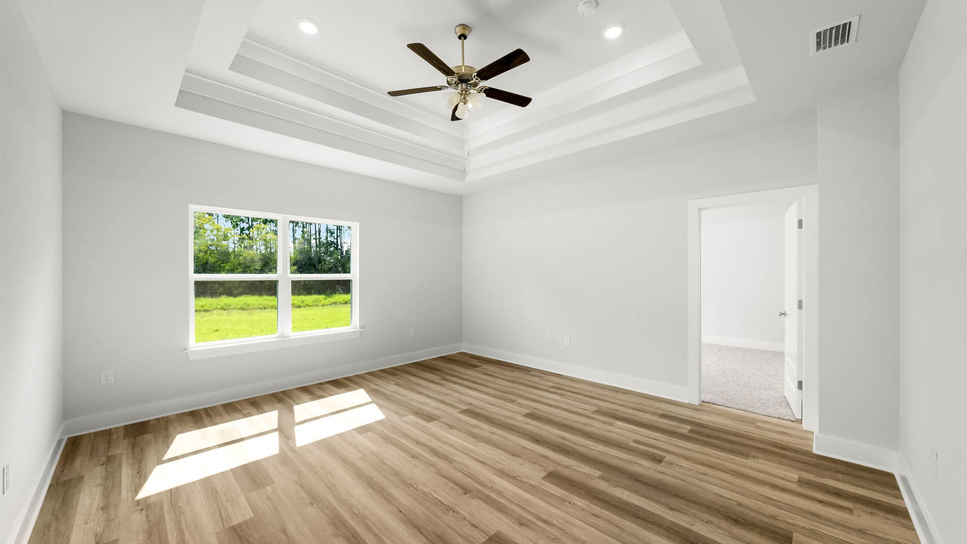 Living room with EVP flooring and tray ceilings and ceiling fan and two windows.