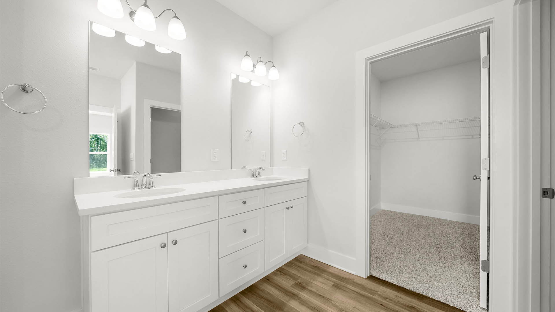 Primary bathroom with double vanity quartz countertops and EVP flooring and white cabinets and walk-in closet.