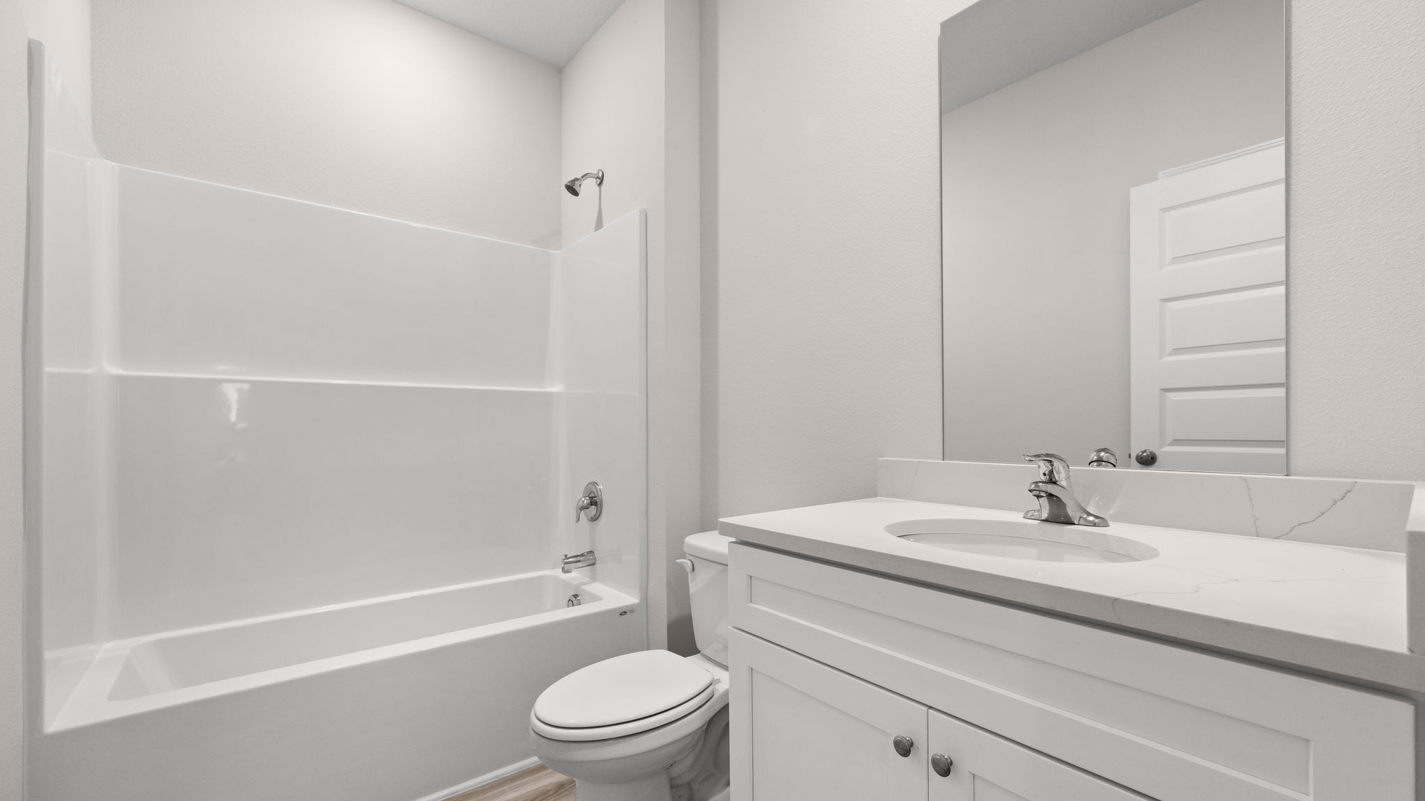Bathroom with single vanity sink and quartz countertops with white cabinets and EVP flooring and shower and toilet.