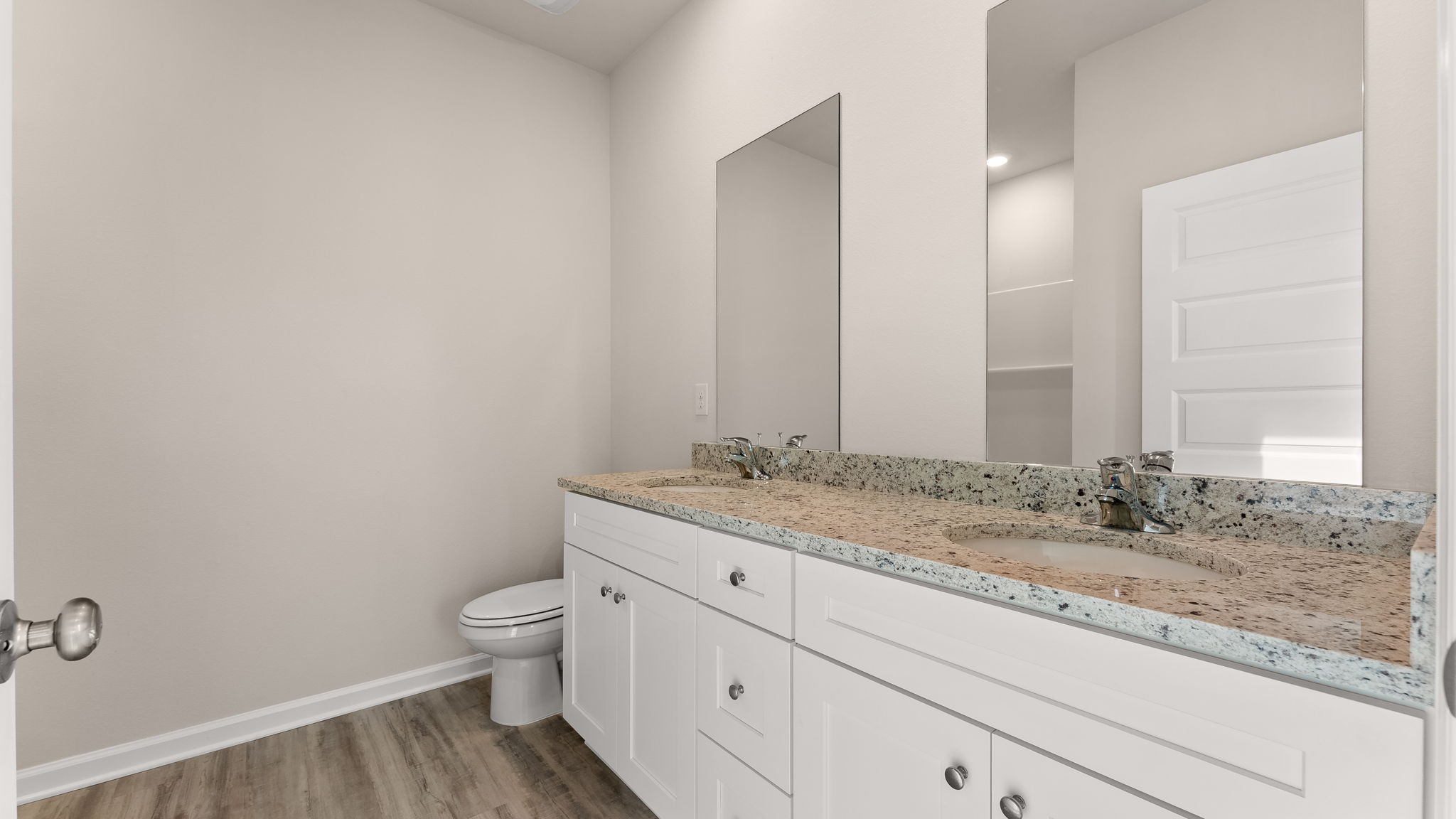 Primary bathroom with double vanity sink and granite countertops with white cabinets and EVP flooring and shower and toilet.