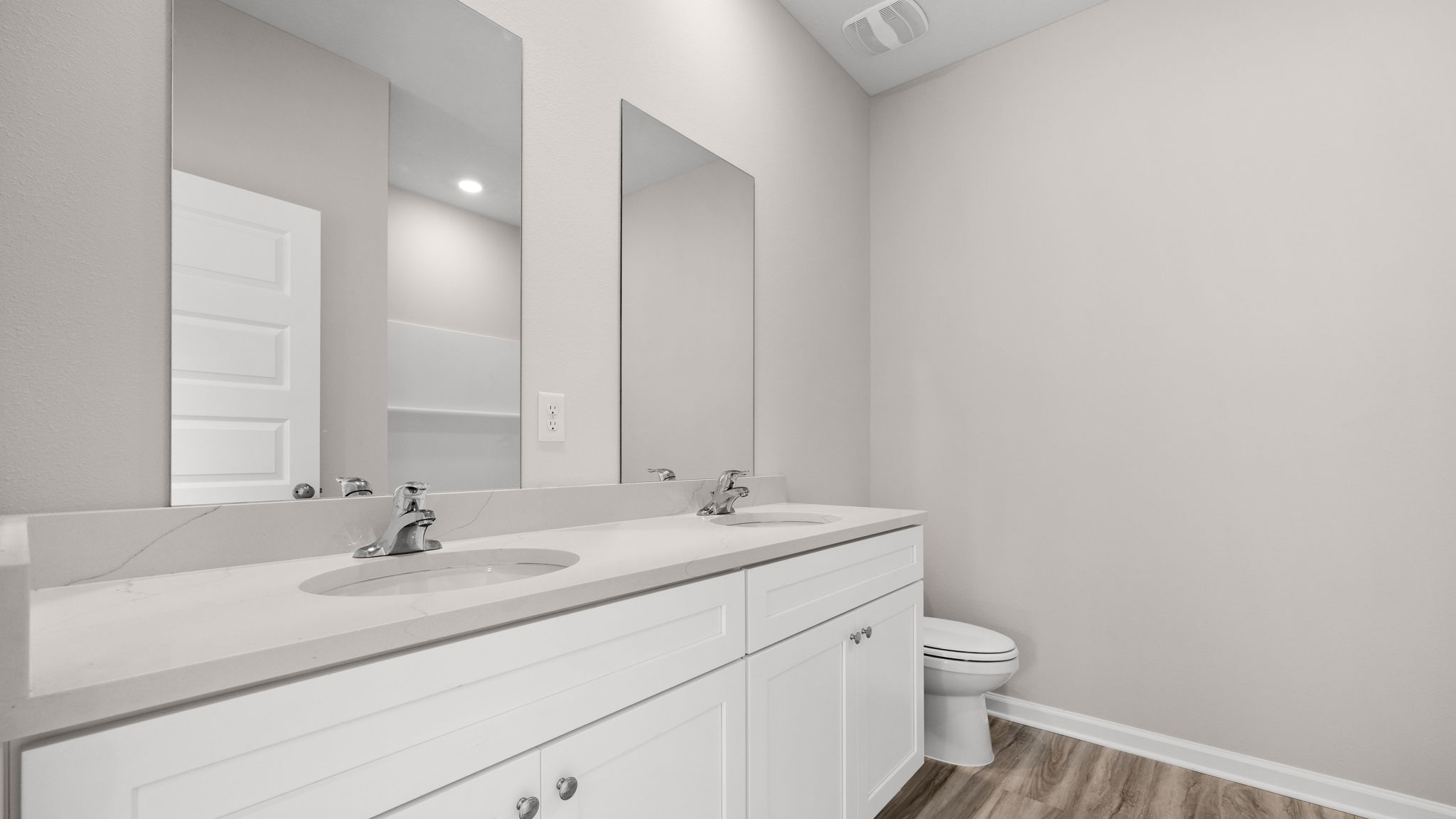 Primary bathroom with double vanity sink and quartz countertops with white cabinets and EVP flooring and shower and toilet.