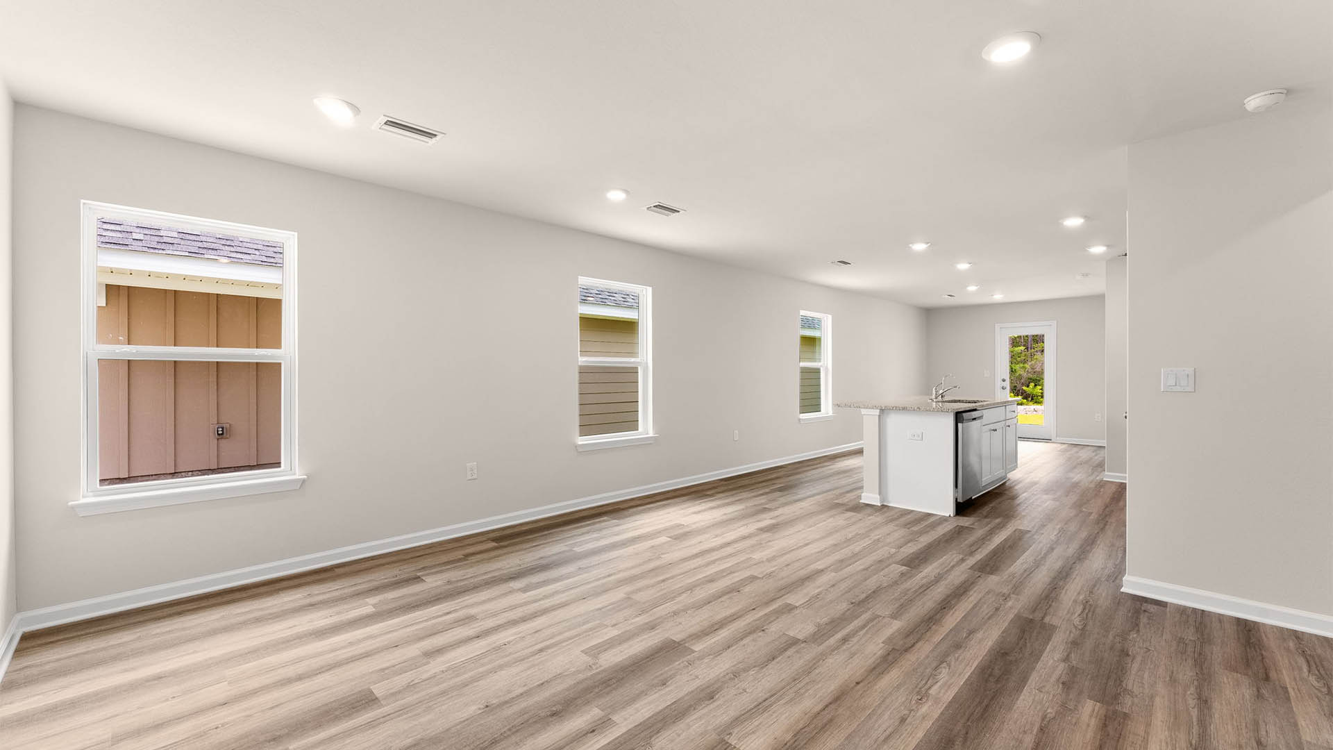 Open living room and kitchen with EVP flooring and 3 windows.