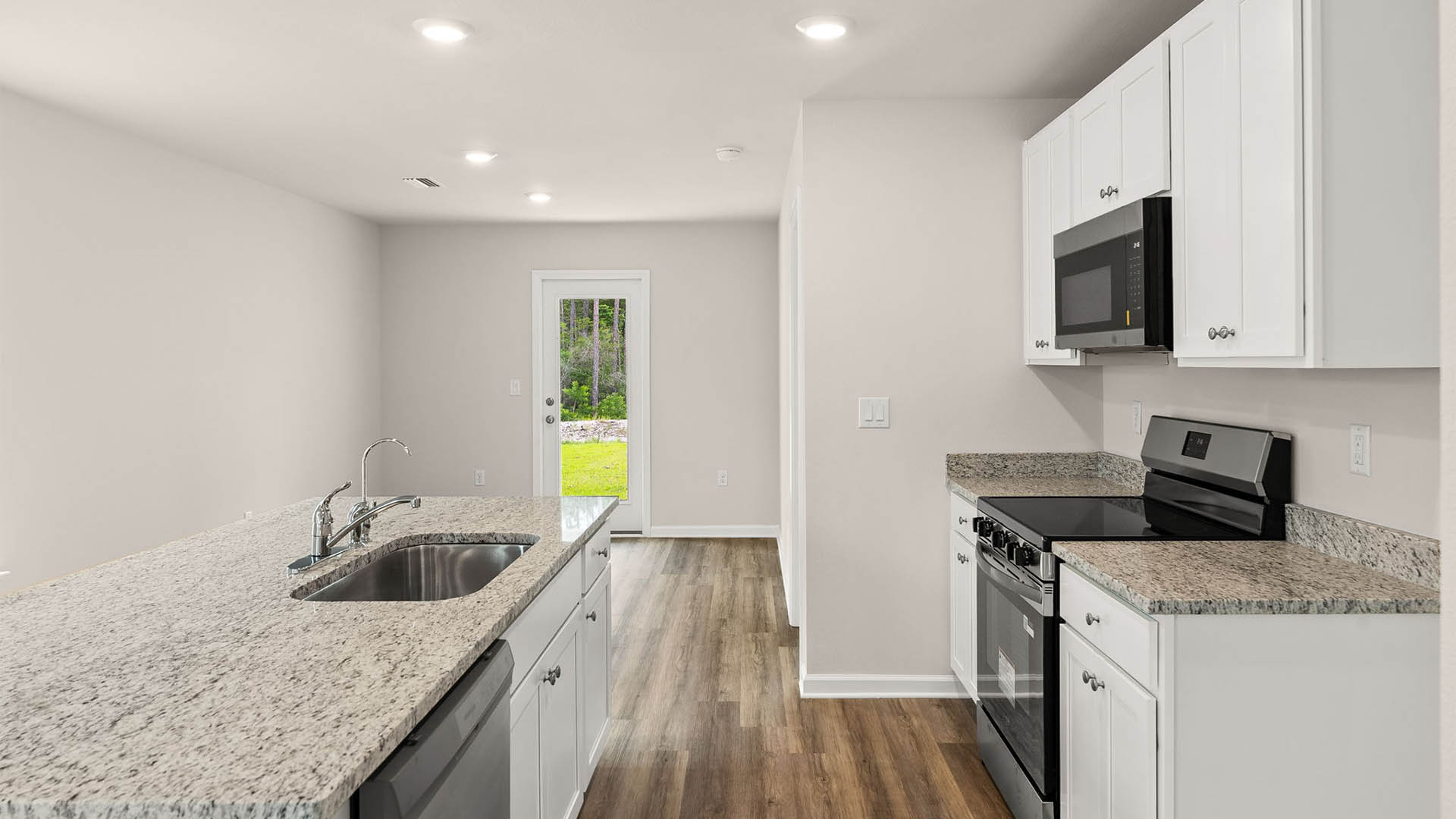 Open kitchen with center island with granite countertops and stainless-steel appliances and closet pantry and white cabinets.