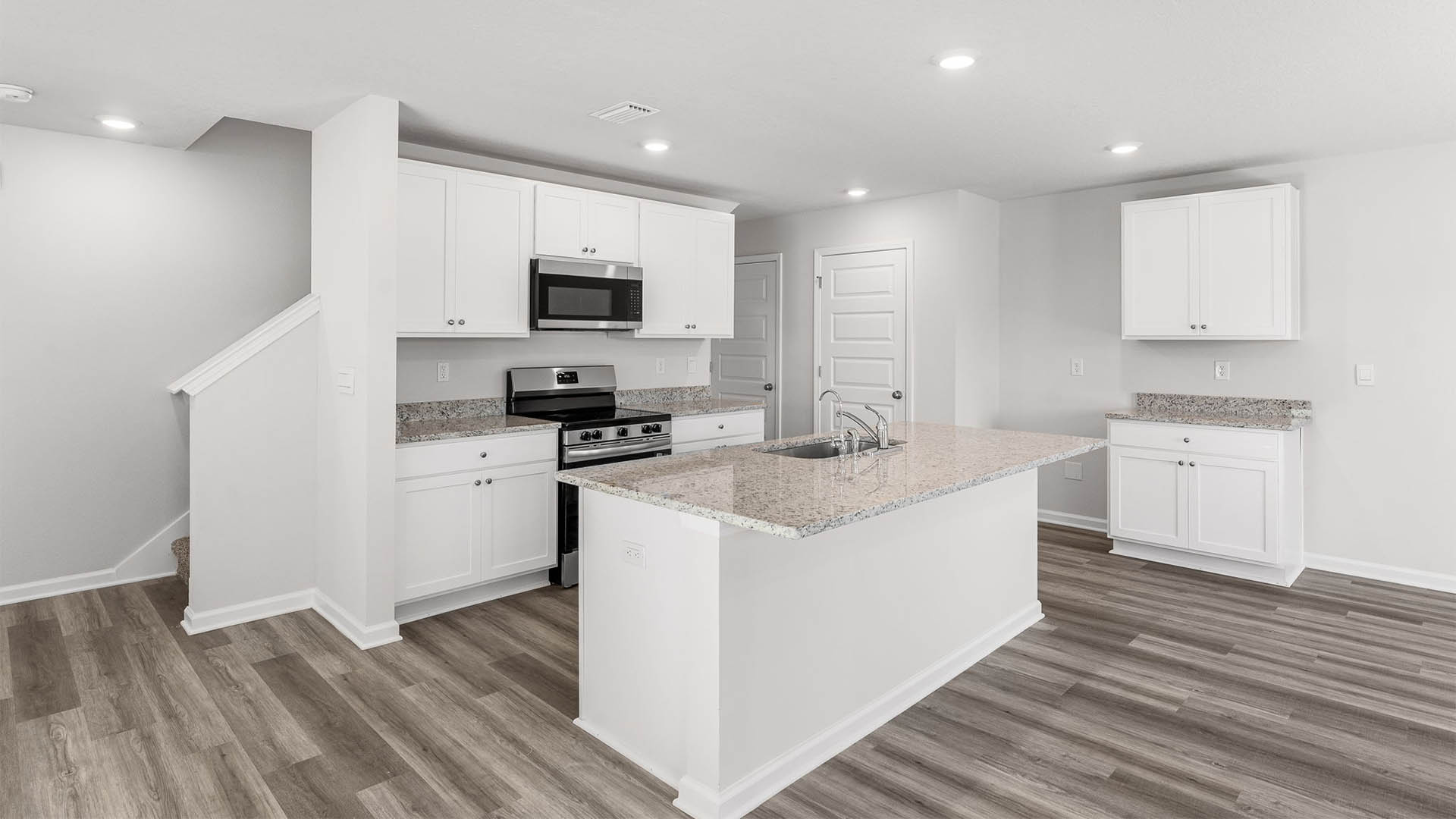 Kitchen with island and granite countertops and white cabinetry and stainless-steel appliances.