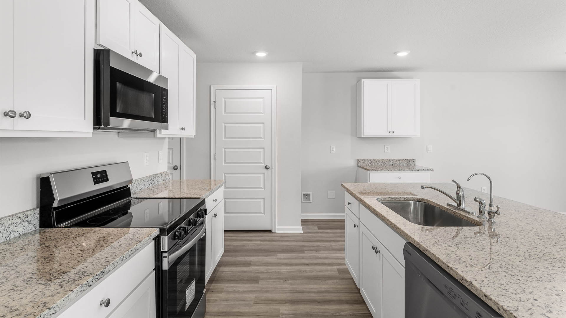 Kitchen with island and granite countertops and white cabinetry and stainless-steel appliances.
