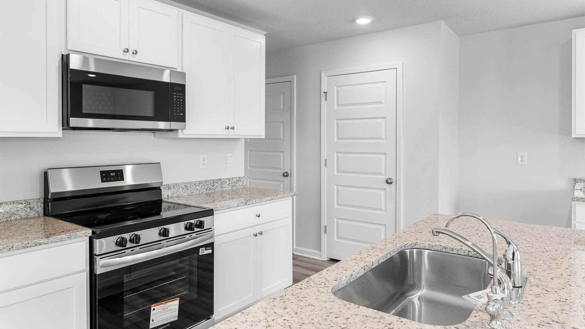 Kitchen with island and granite countertops and white cabinetry and stainless-steel appliances.