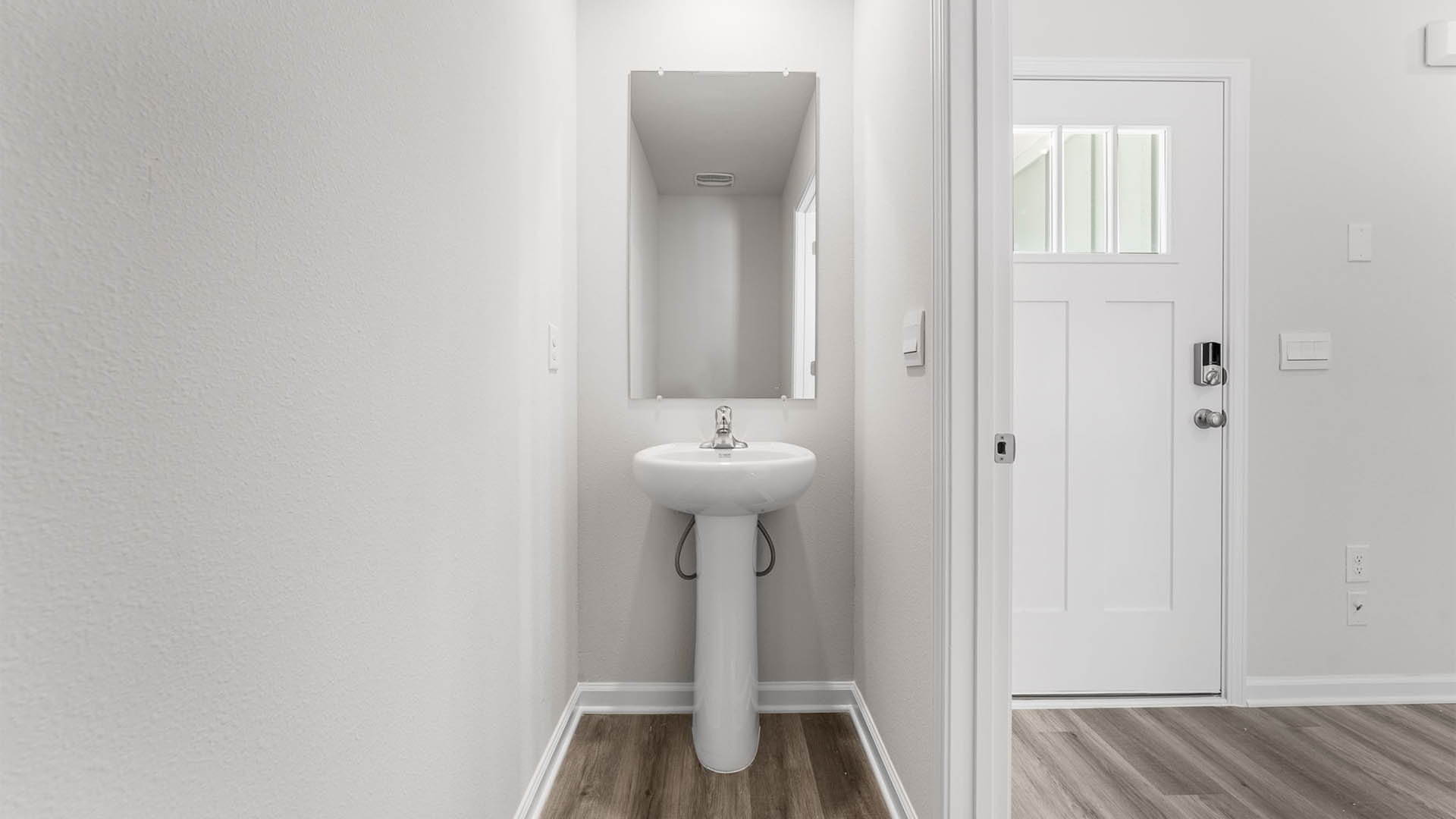 Half-bathroom with EVP flooring and sink and mirror next to front door.