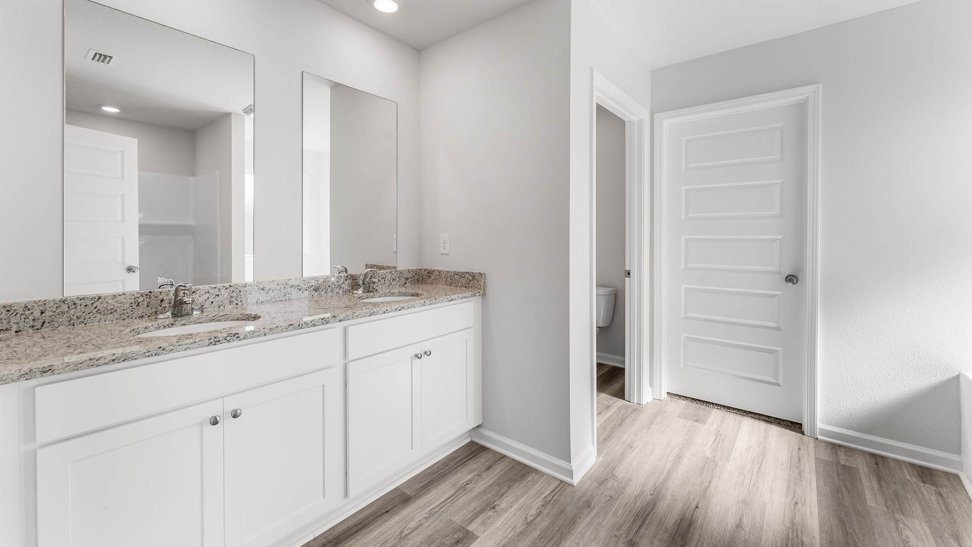 Primary bathroom with double vanity granite countertops and closet entrance.