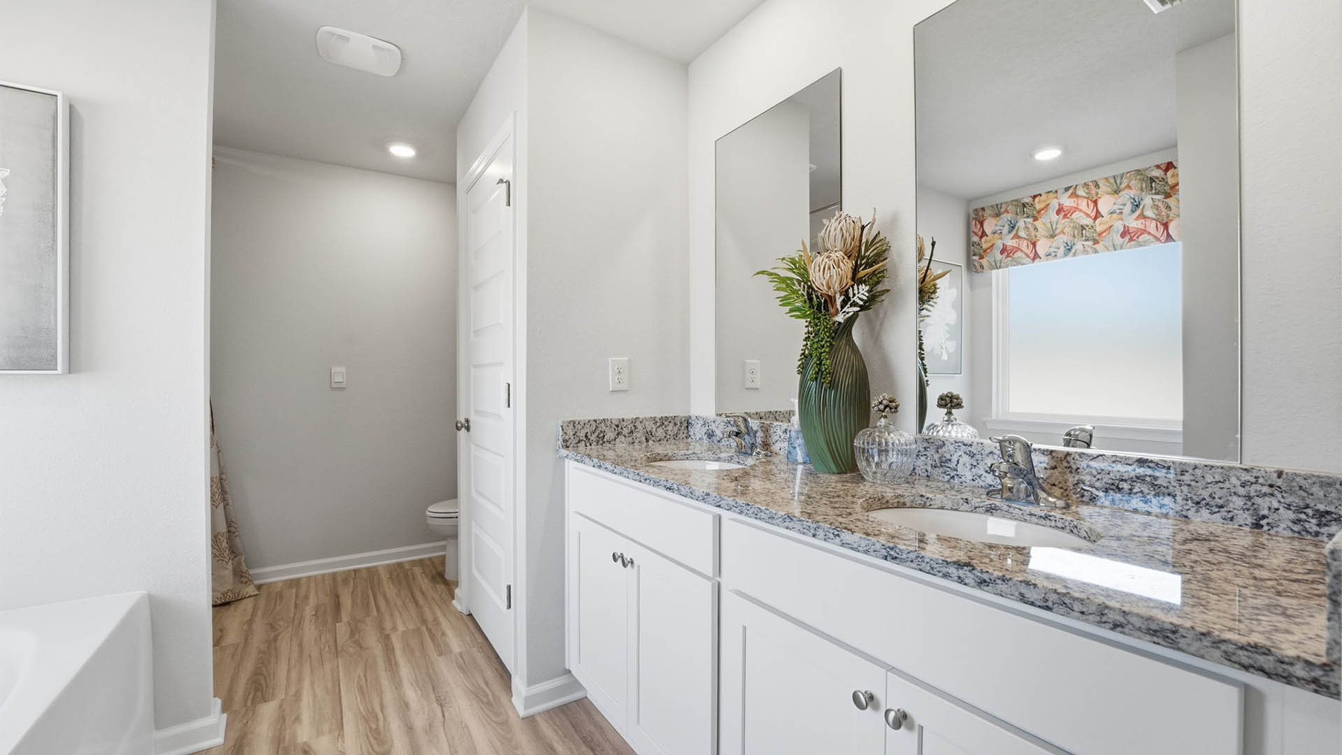 Primary bathroom with double vanity sink and granite countertops and tub and closet.