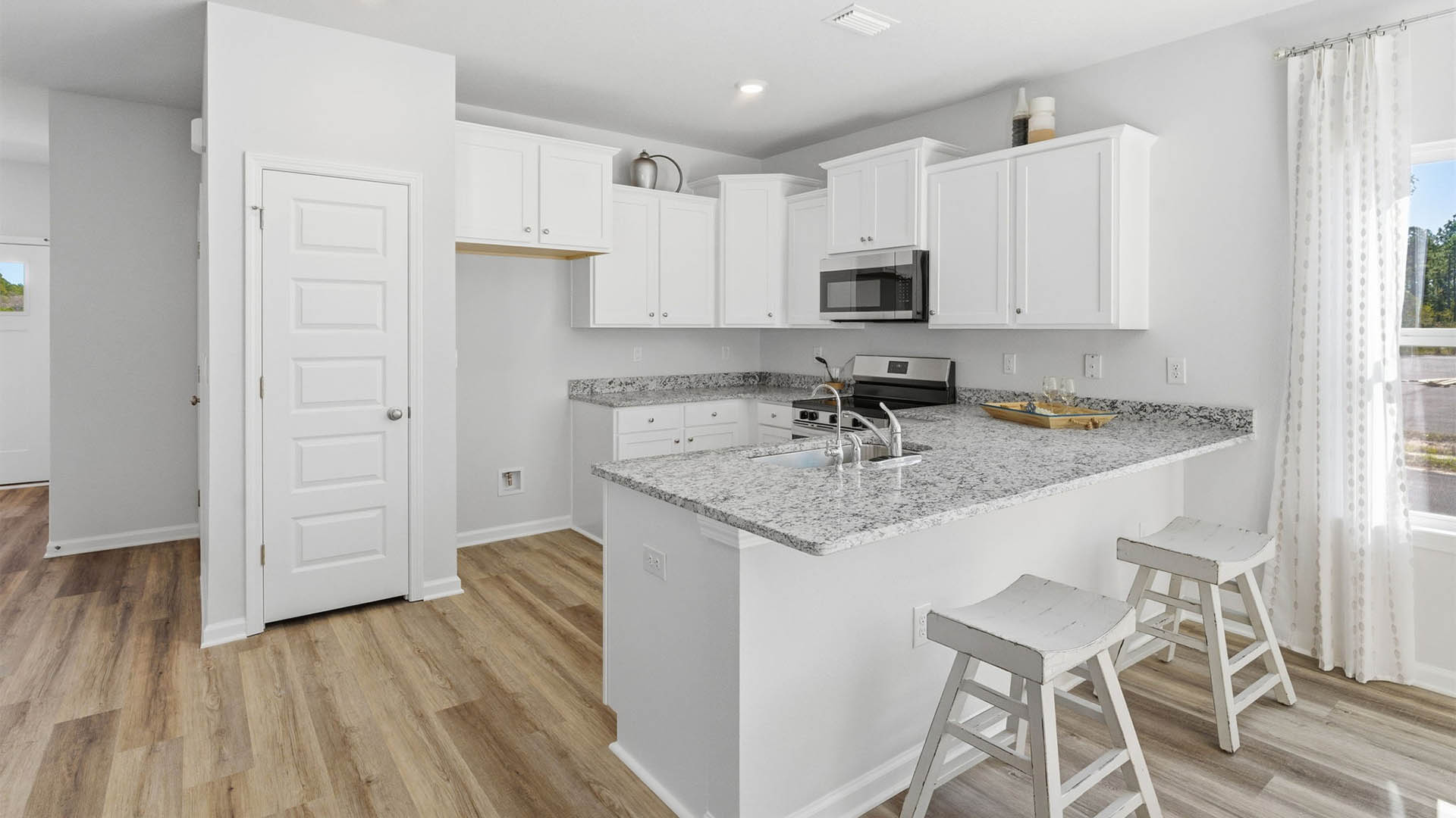 Kitchen with white cabinets and granite countertops and stainless-steel appliances and peninsula bar and pantry.
