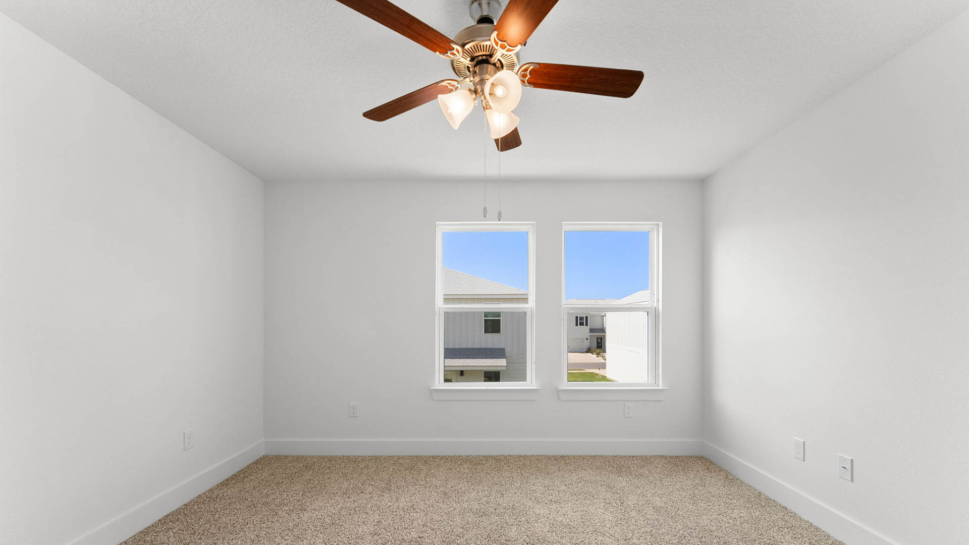 Primary bedroom with ceiling fan and carpet flooring and two windows.