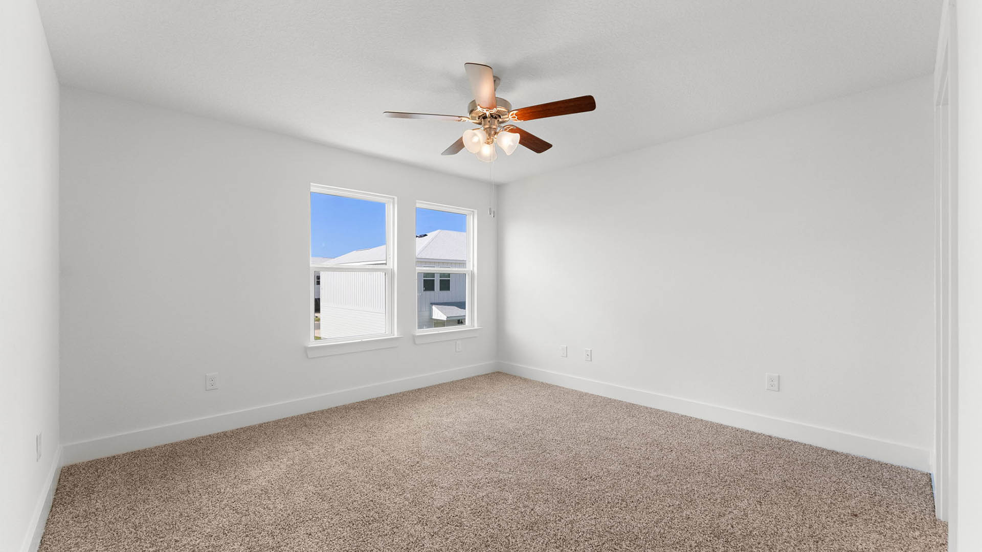 Primary bedroom with ceiling fan and carpet flooring and two windows.