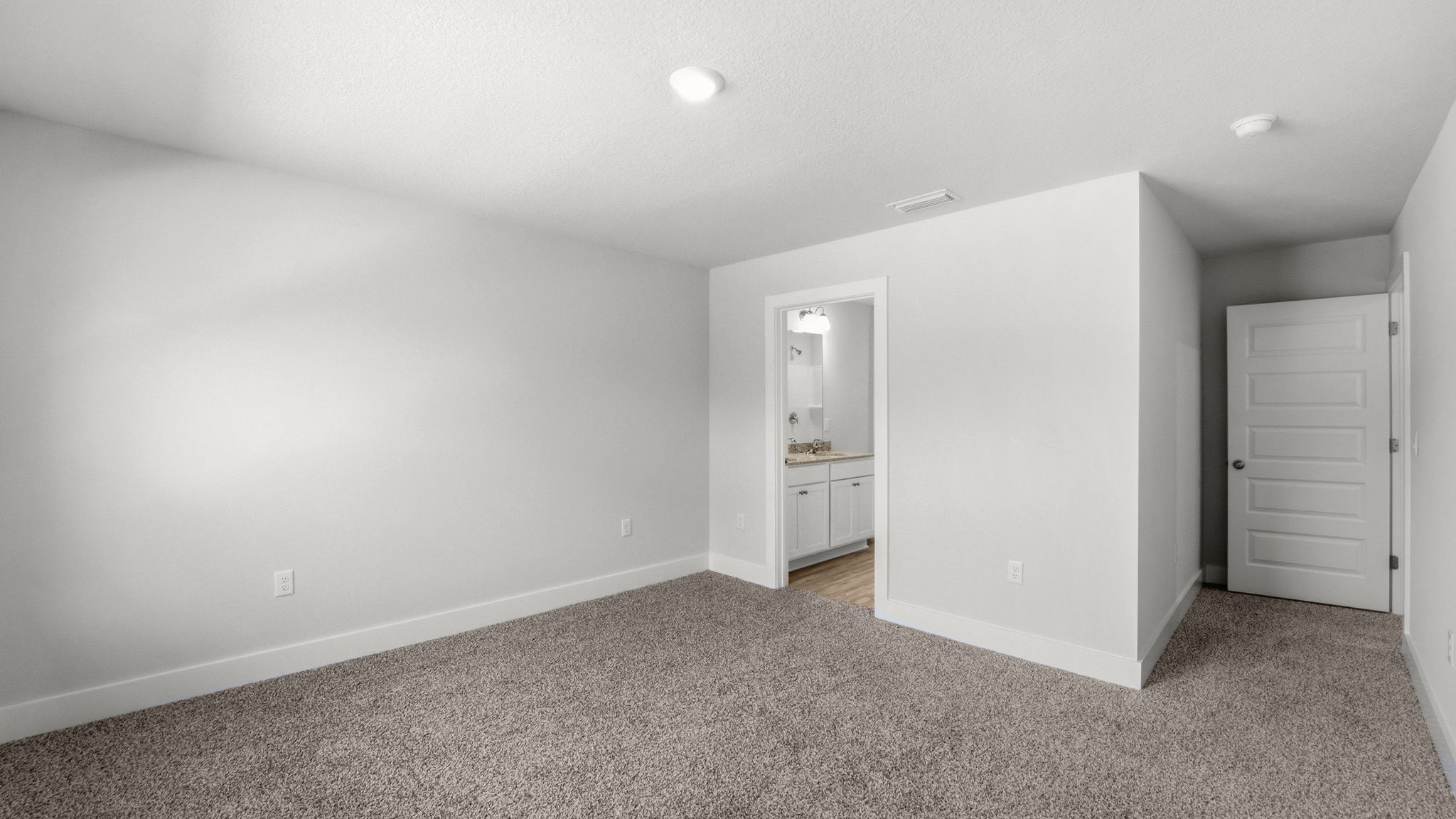 Primary bedroom with ceiling fan and carpet flooring and bathroom entrance.