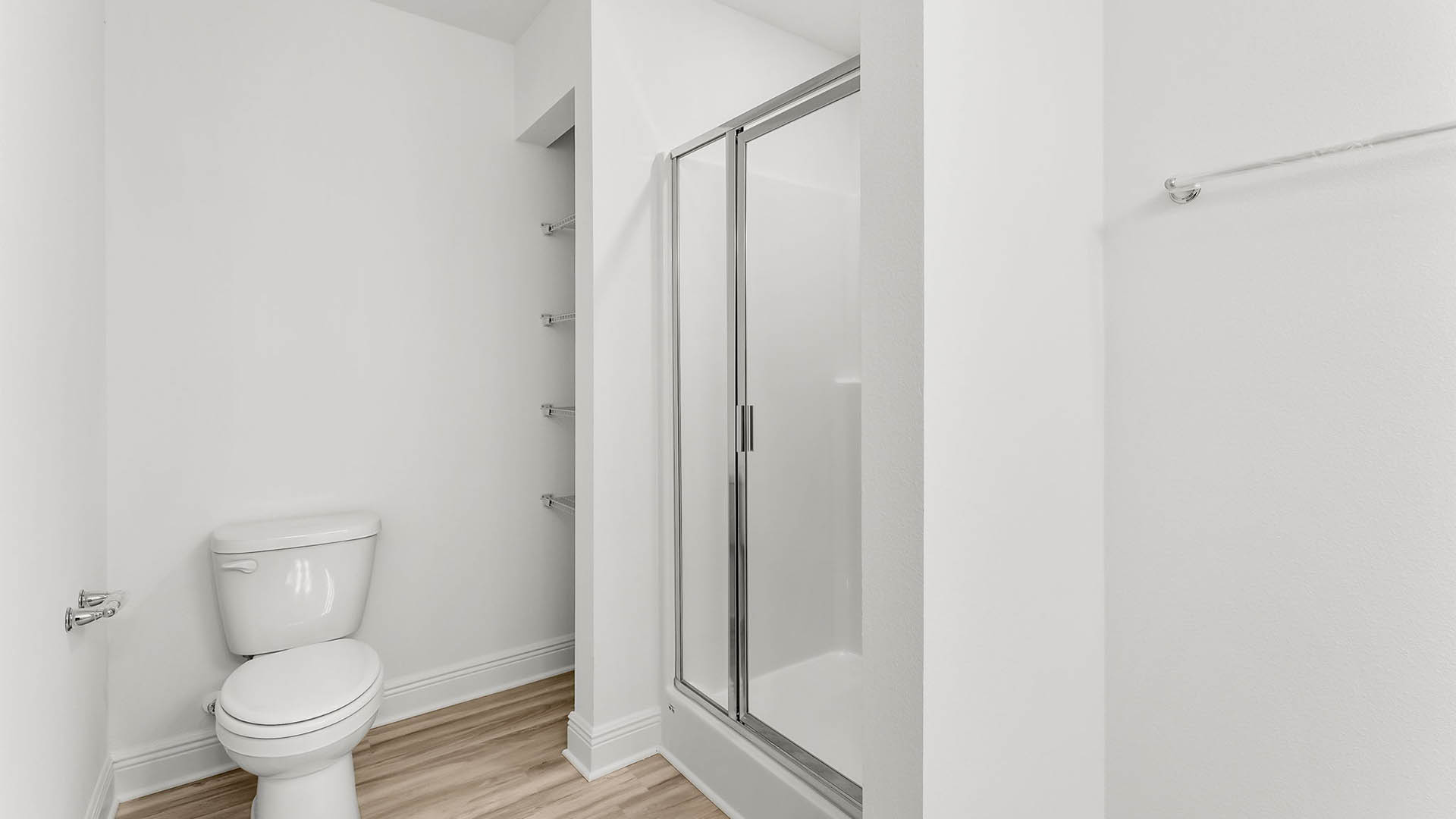 Primary bathroom with shower with glass doors and toilet and shelving.