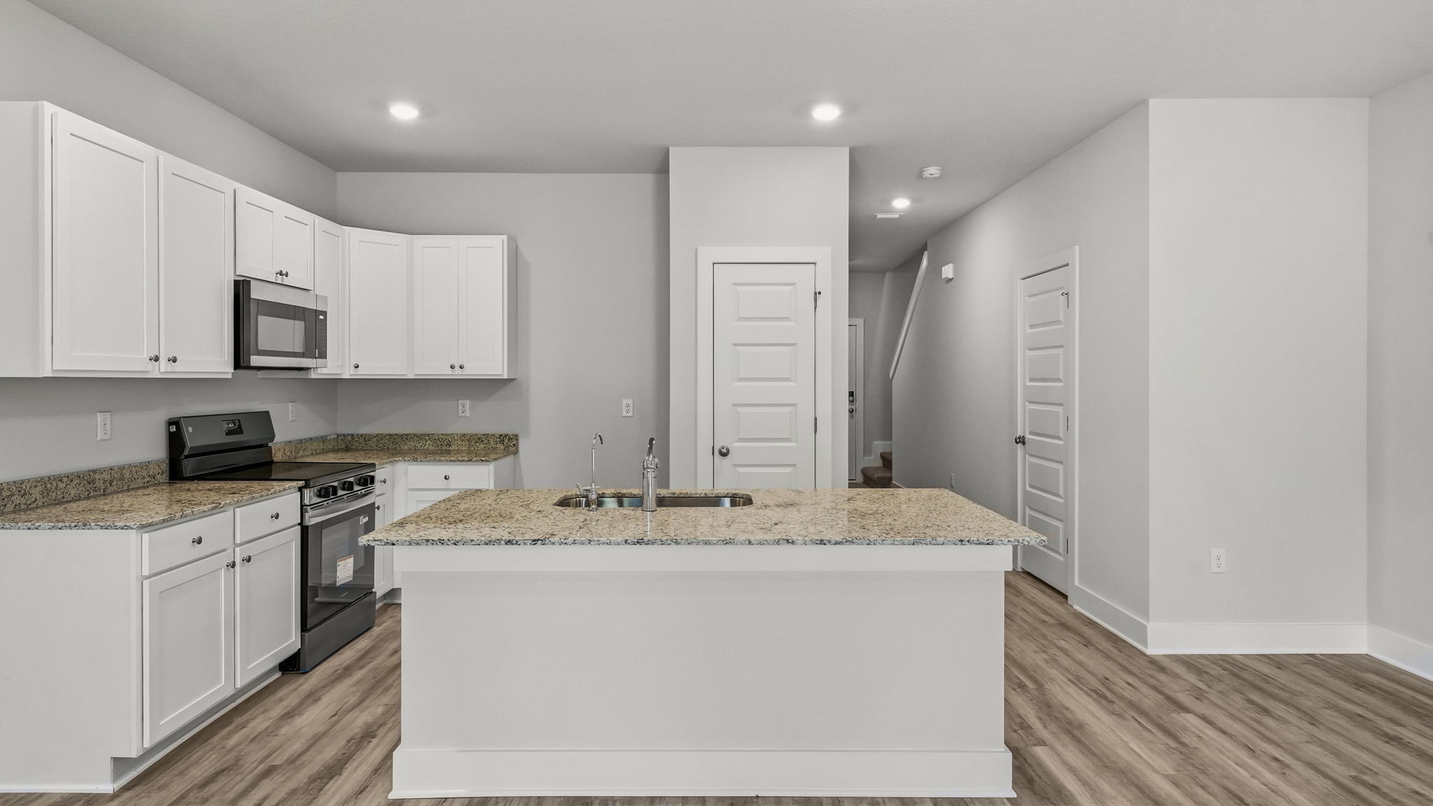 Kitchen with granite countertops and stainless-steel appliances and island and white cabinets.