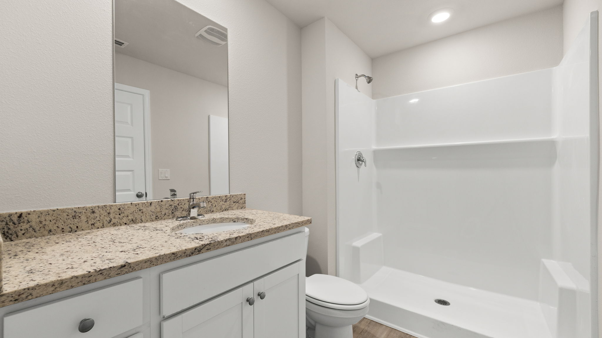 Bathroom with granite countertops and white cabinets and single vanity sinks and toilet and shower.