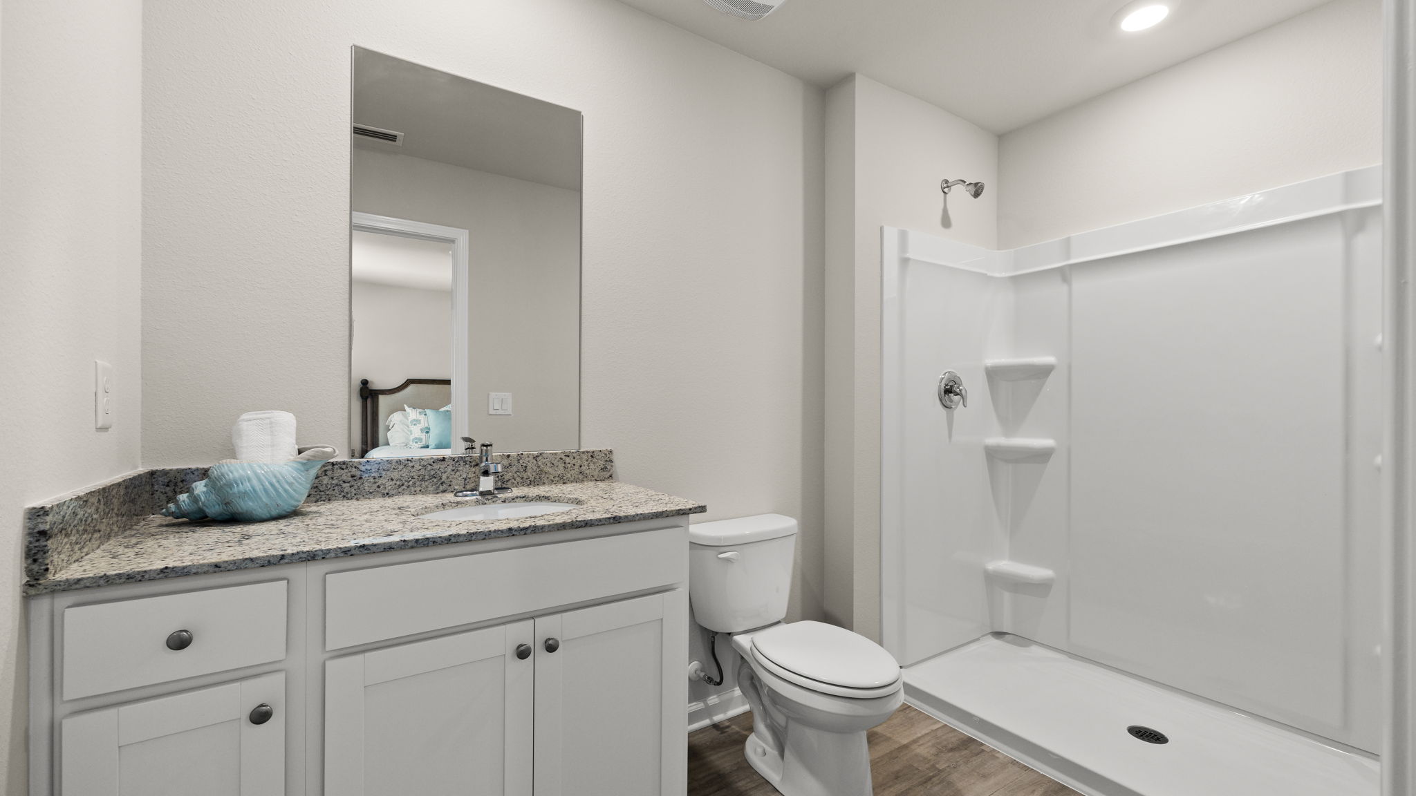Primary bathroom with granite countertops and white cabinets and single vanity sinks and toilet and shower.