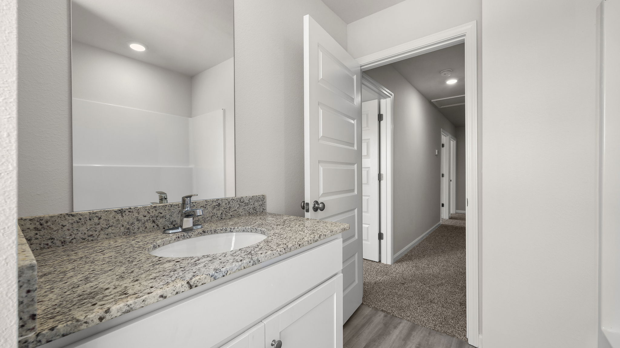Primary bathroom with granite countertops and white cabinets and single vanity sink.