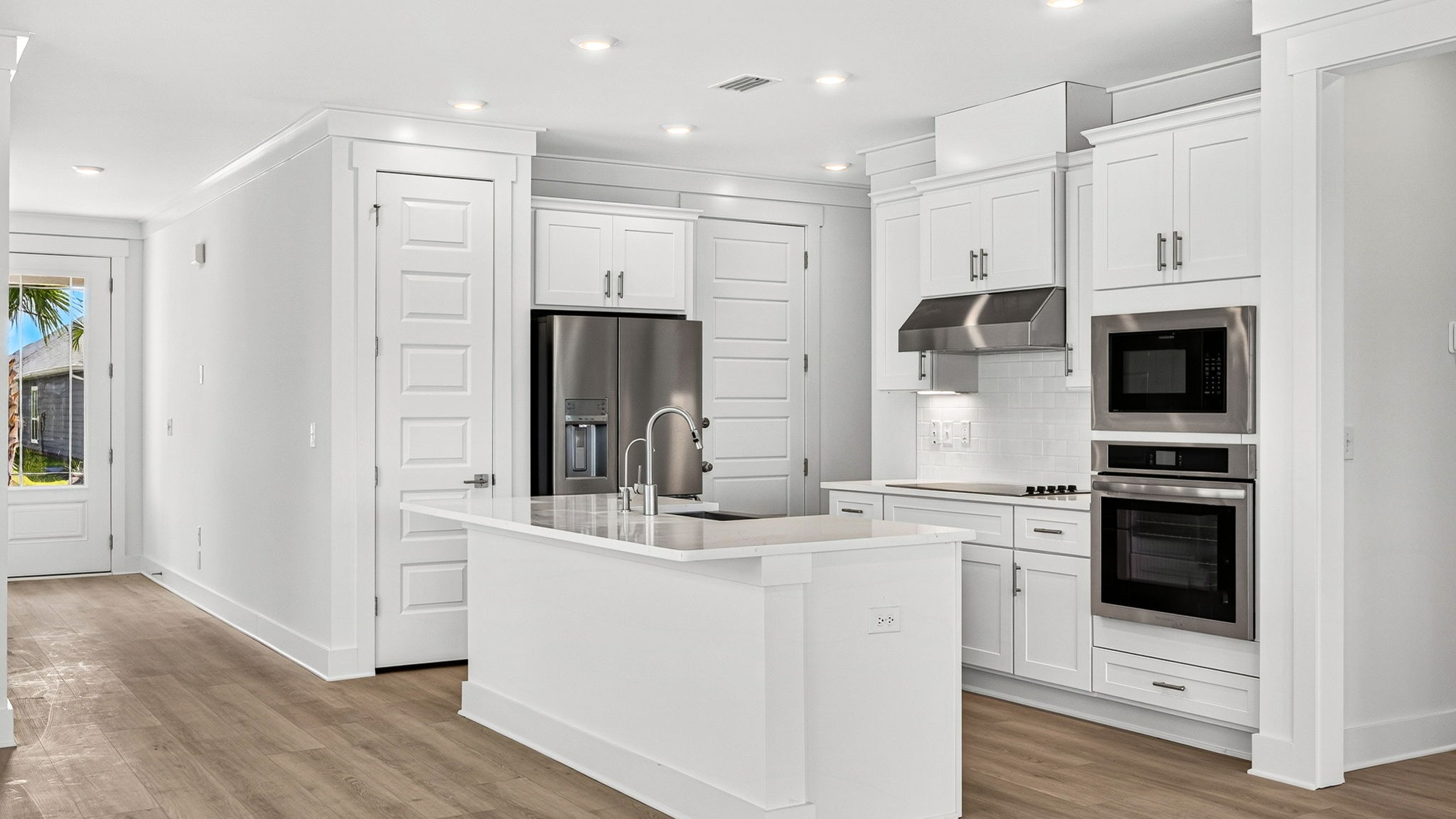 Open kitchen with island with quartz countertops and stainless-steel appliances and pantry.