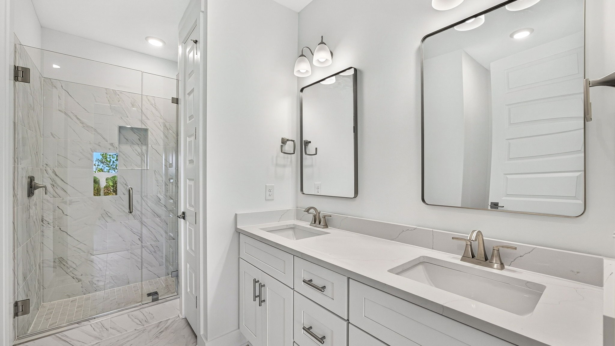 Primary bathroom with double vanity quartz countertops with white cabinets and florentine tile shower with glass door.