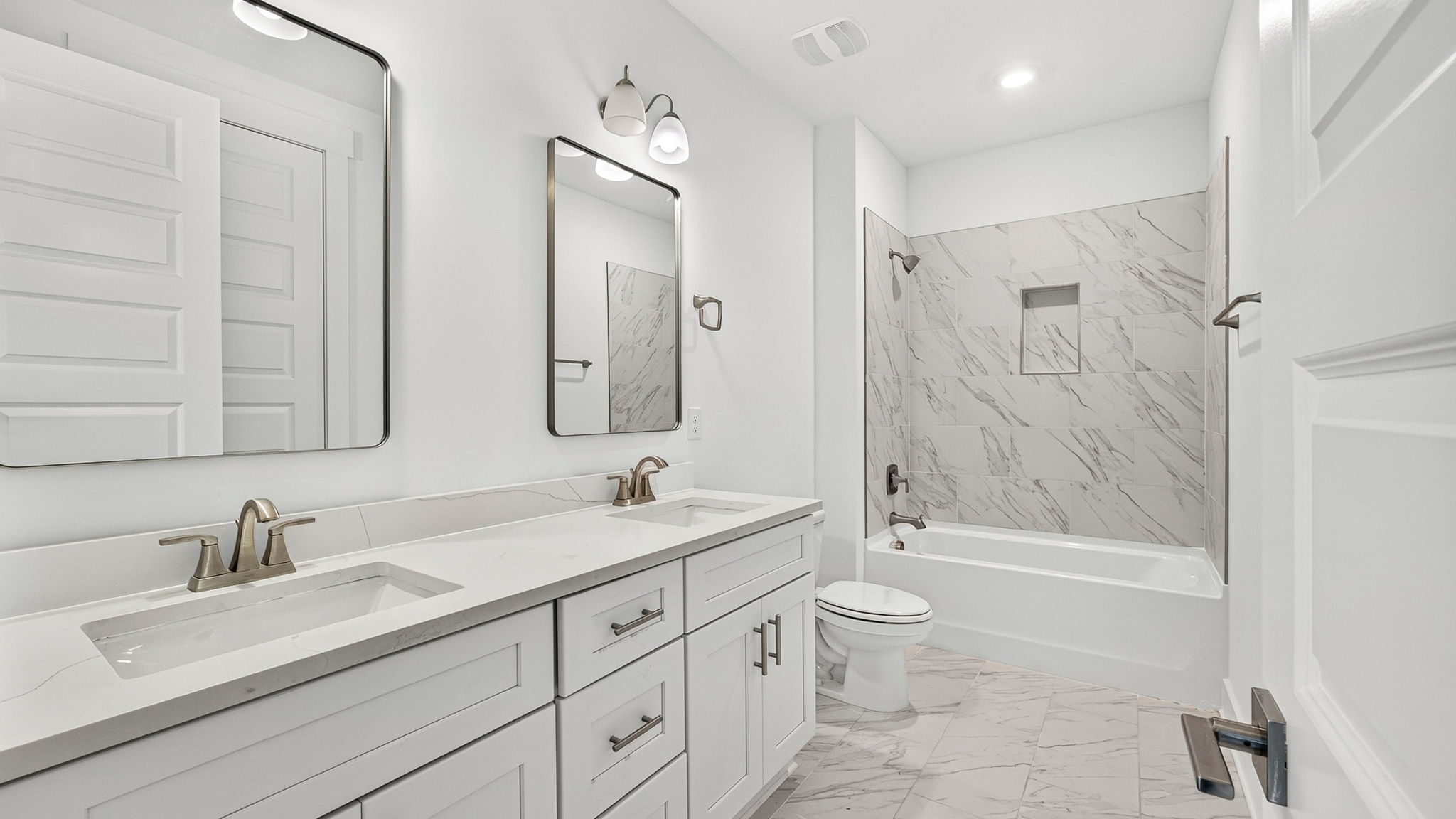 Bathroom with double vanity quartz countertops with white cabinets and florentine tiled shower and tub combo.