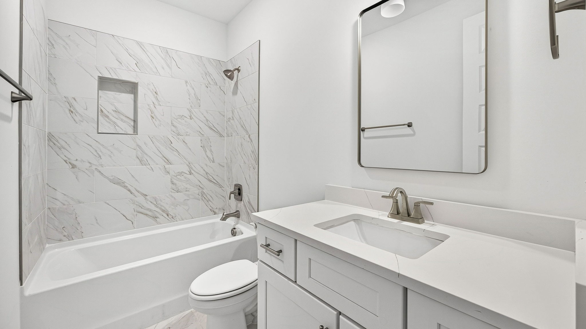 Bathroom with single vanity quartz countertops with white cabinets and florentine tiled shower and tub combo.