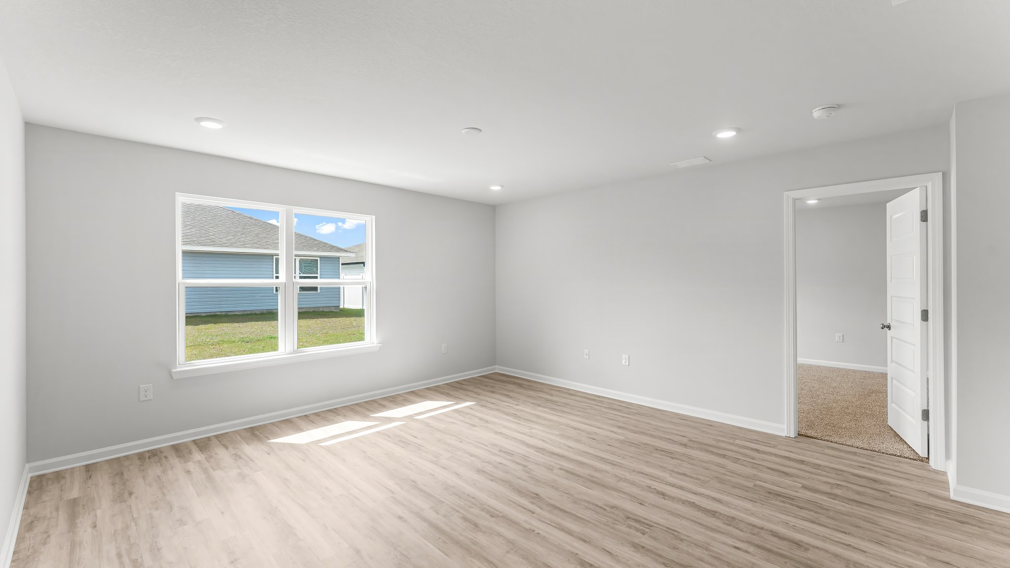 Open living room with EVP flooring and two windows next to primary bedroom entrance.